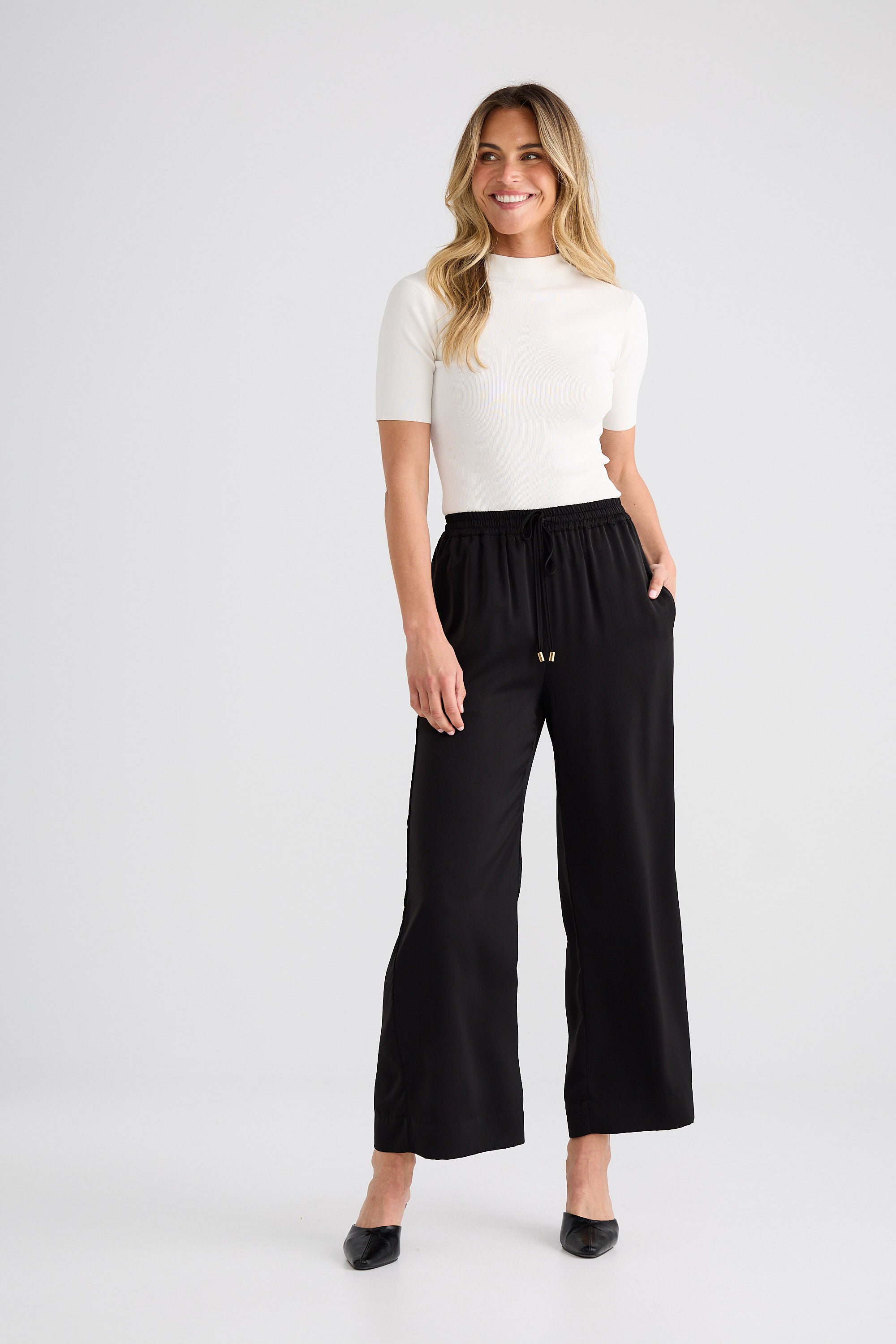 Woman wearing a white top and black wide-leg pants on a white background