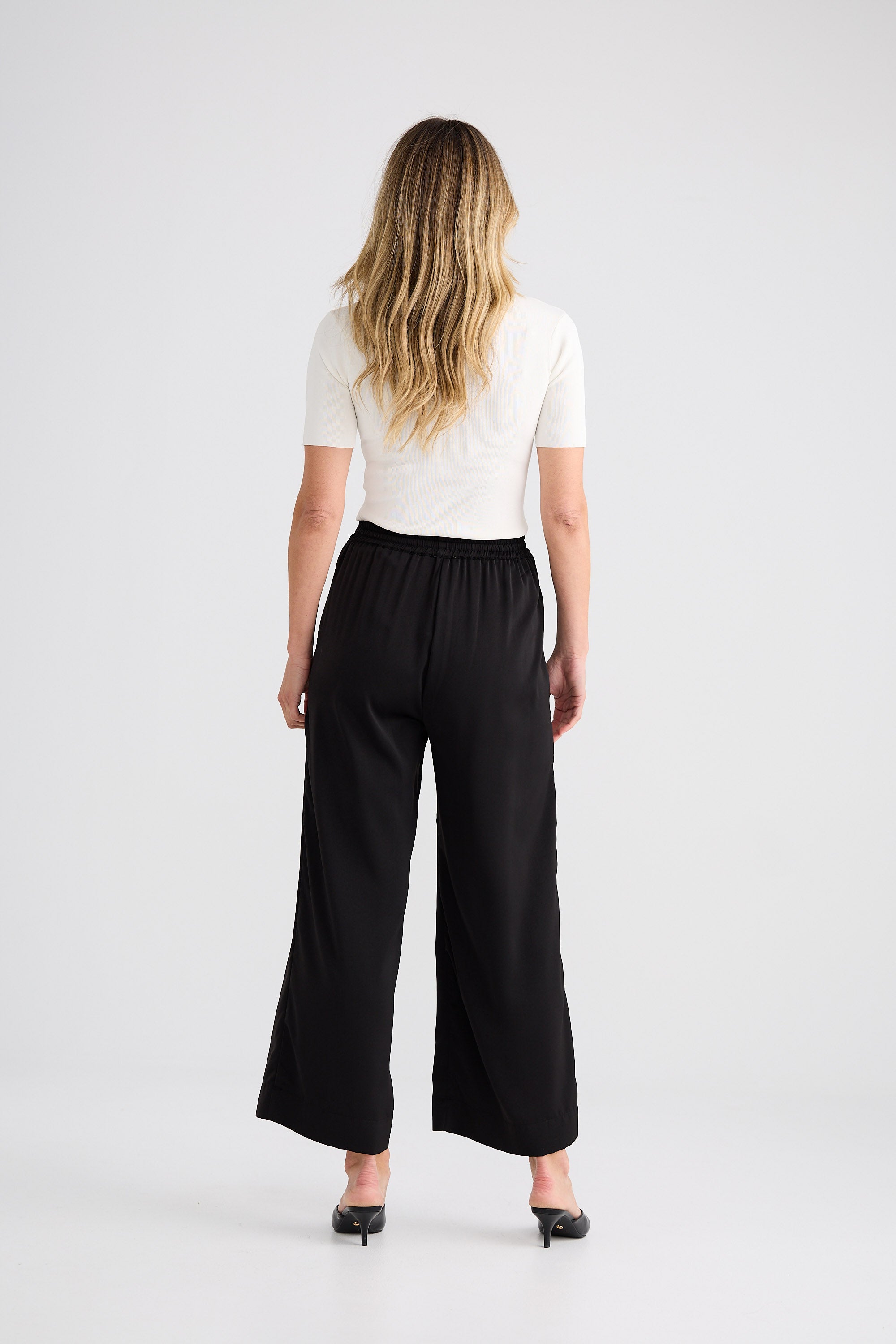 Person wearing a white top and black wide-leg pants on a plain background