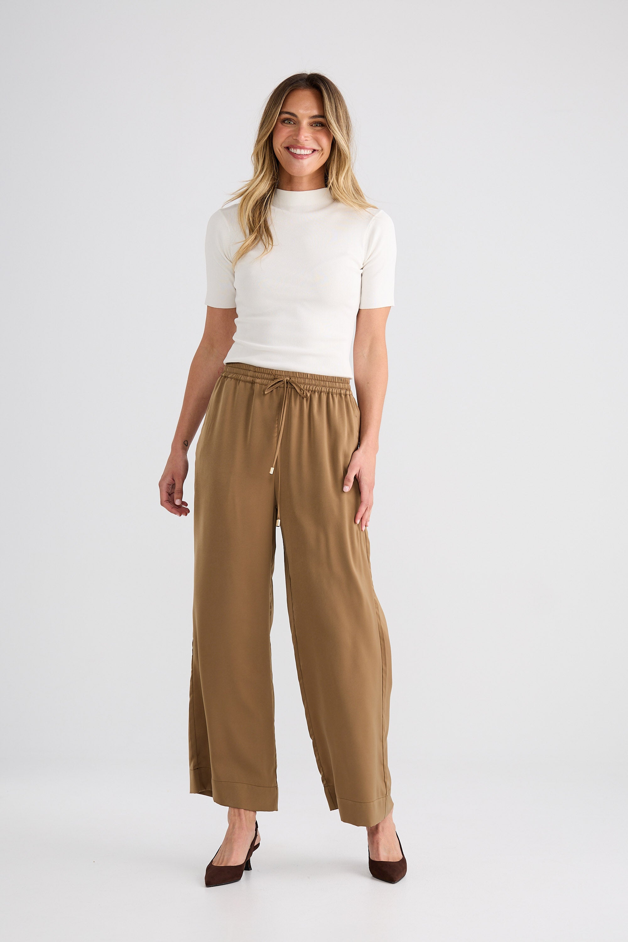 Woman wearing a white top and brown wide-leg pants on a white background