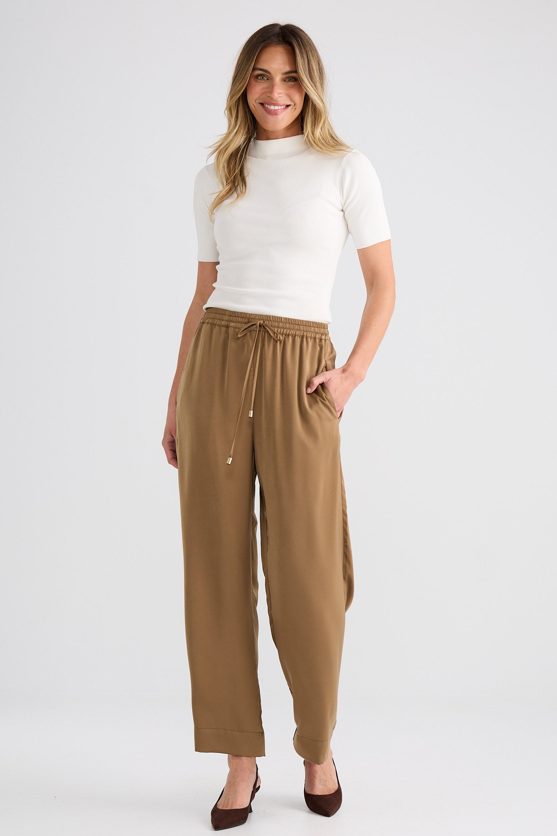 Woman wearing a white top and tan pants on a white background