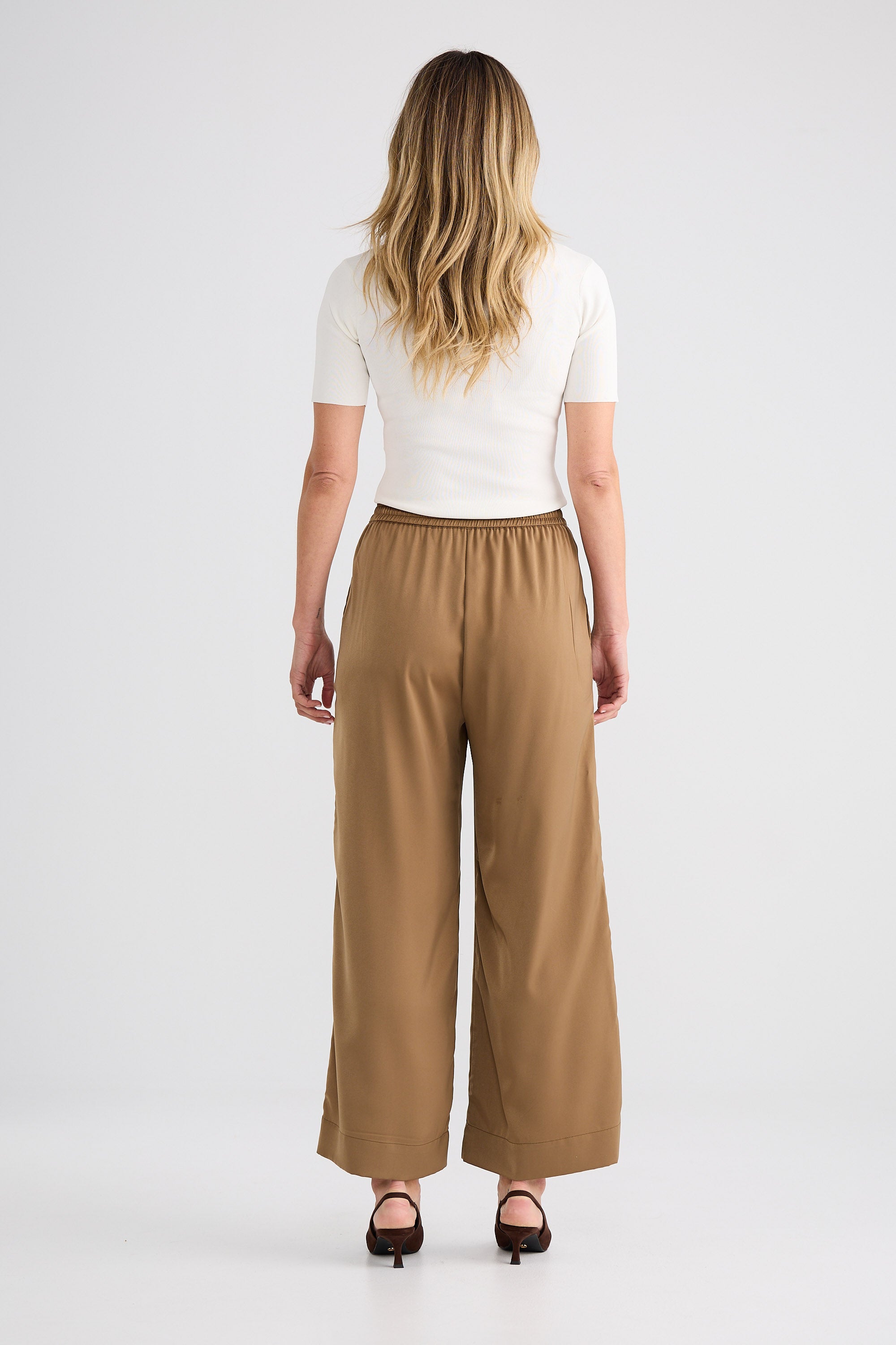 Woman wearing a white top and brown wide-leg pants on a white background