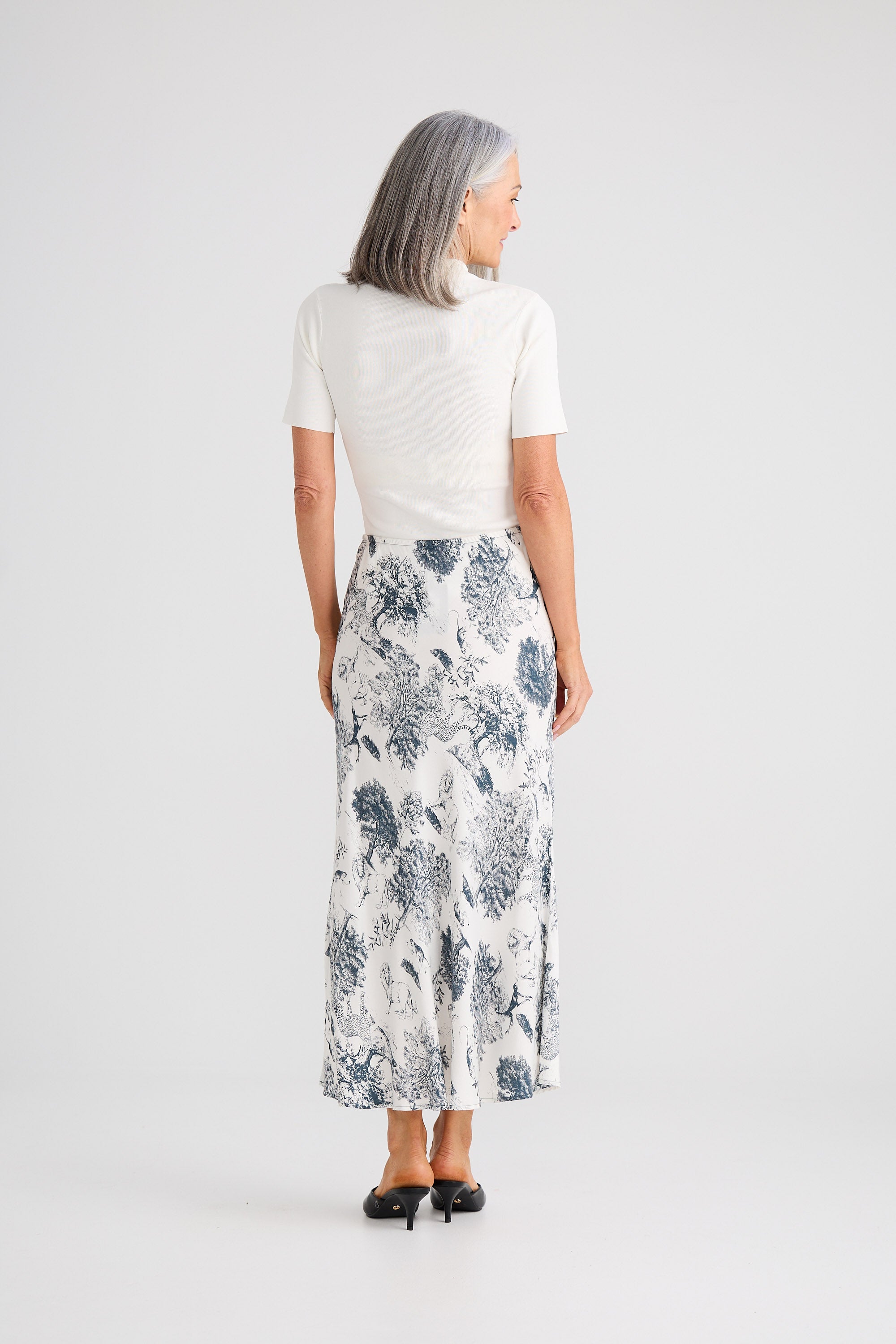 Woman wearing a white top and floral skirt on a plain background