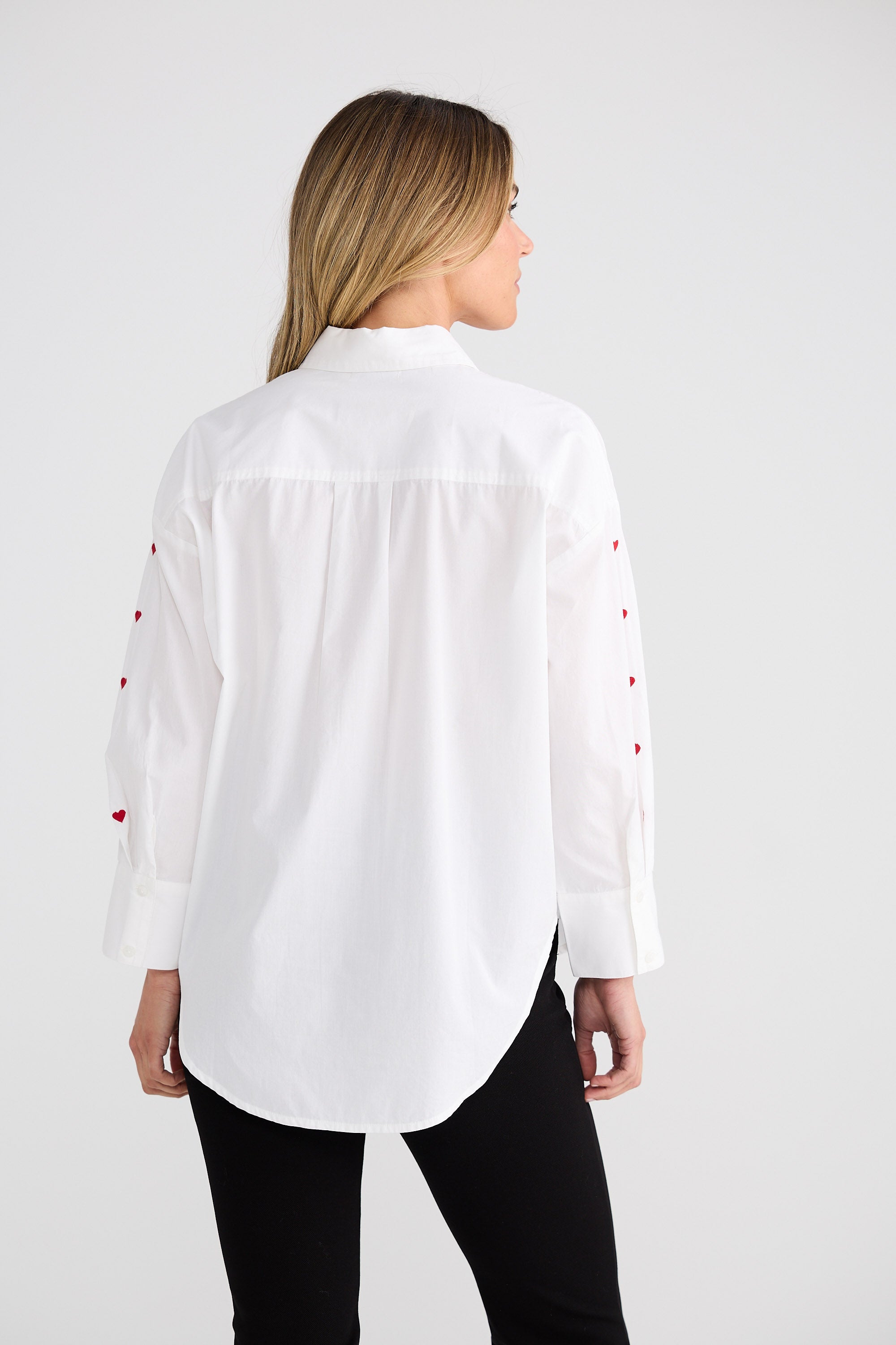 Woman wearing a white blouse with small red heart patterns on a plain background