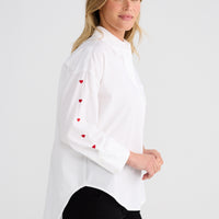 Woman wearing a white blouse with red heart patterns on a plain background