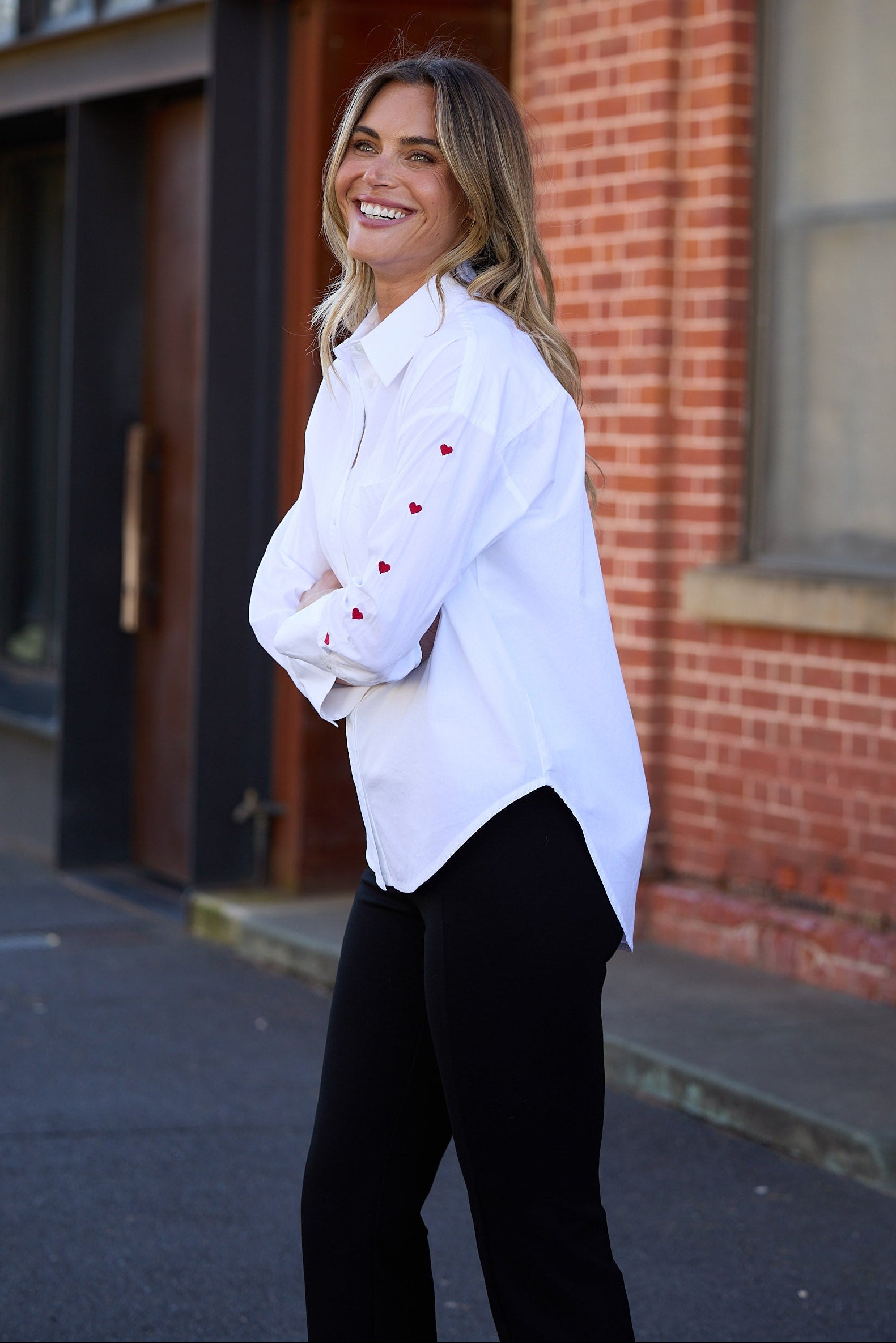 Woman in a white shirt with red buttons standing in front of a brick building.