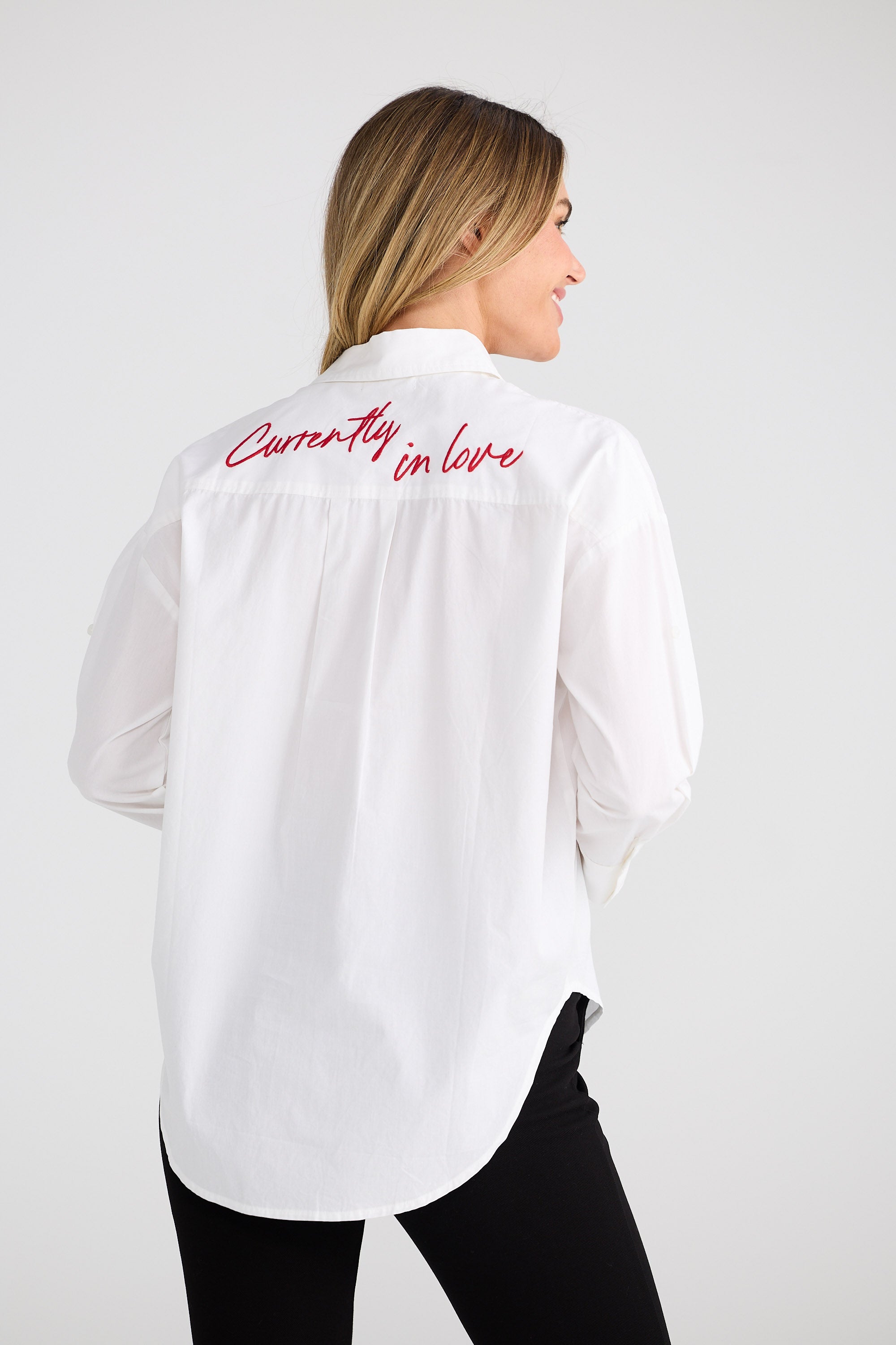 Woman wearing a white shirt with 'Currently in love' text on the back against a white background