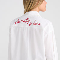White shirt with 'Currently in love' text on the back, worn by a person against a white background