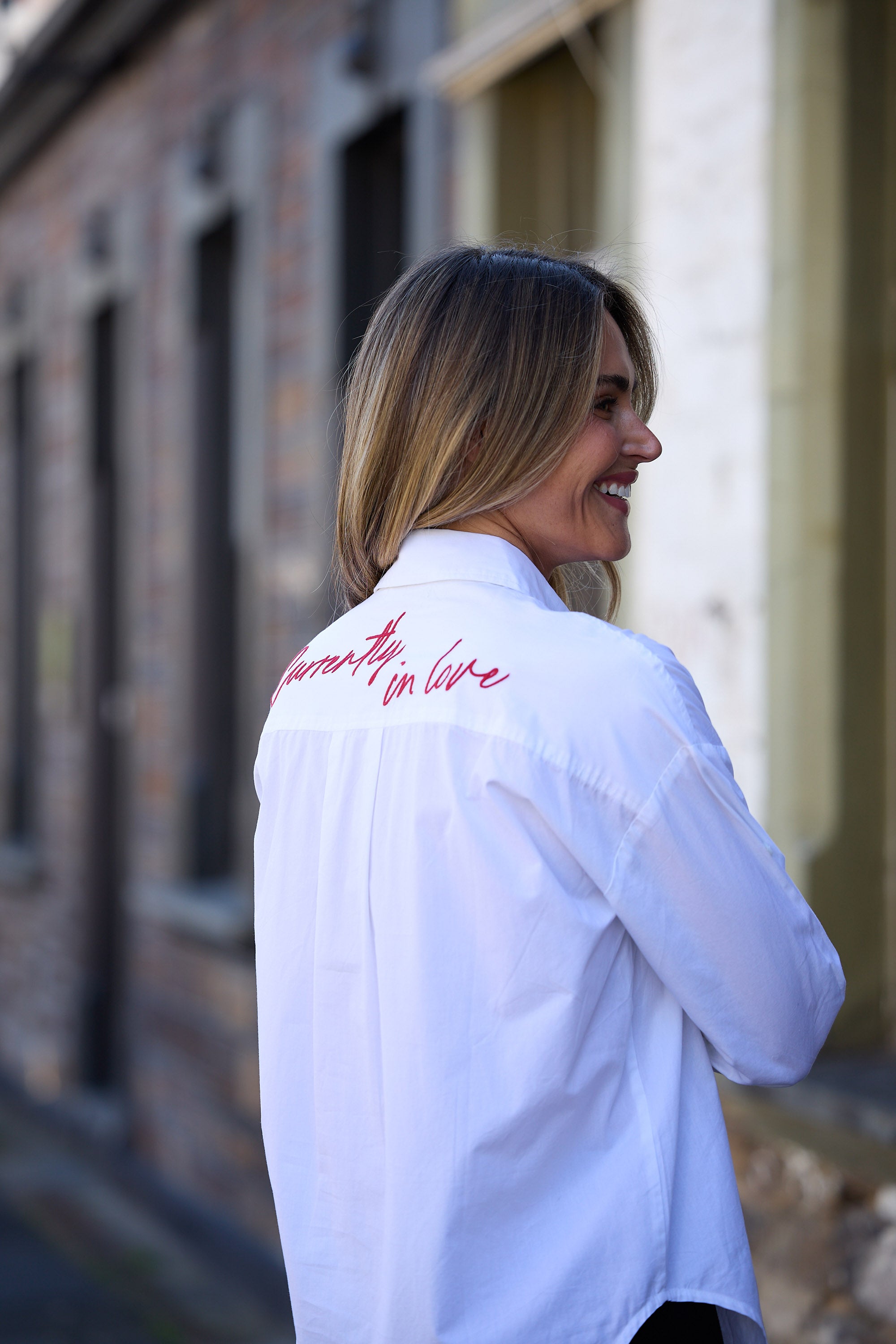 Woman wearing a white shirt with text on the back, standing outdoors.