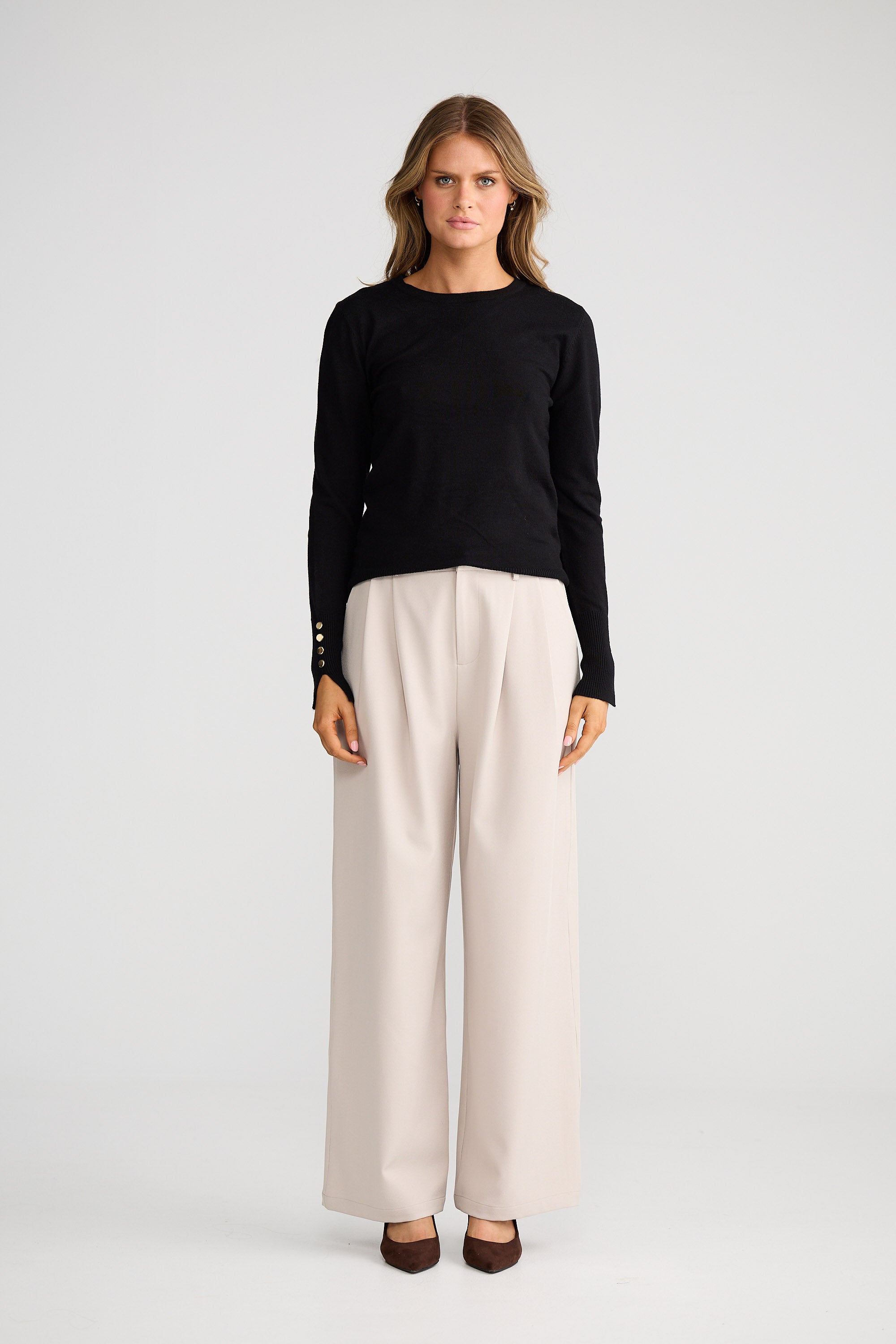 Woman wearing a black top and beige pants on a white background