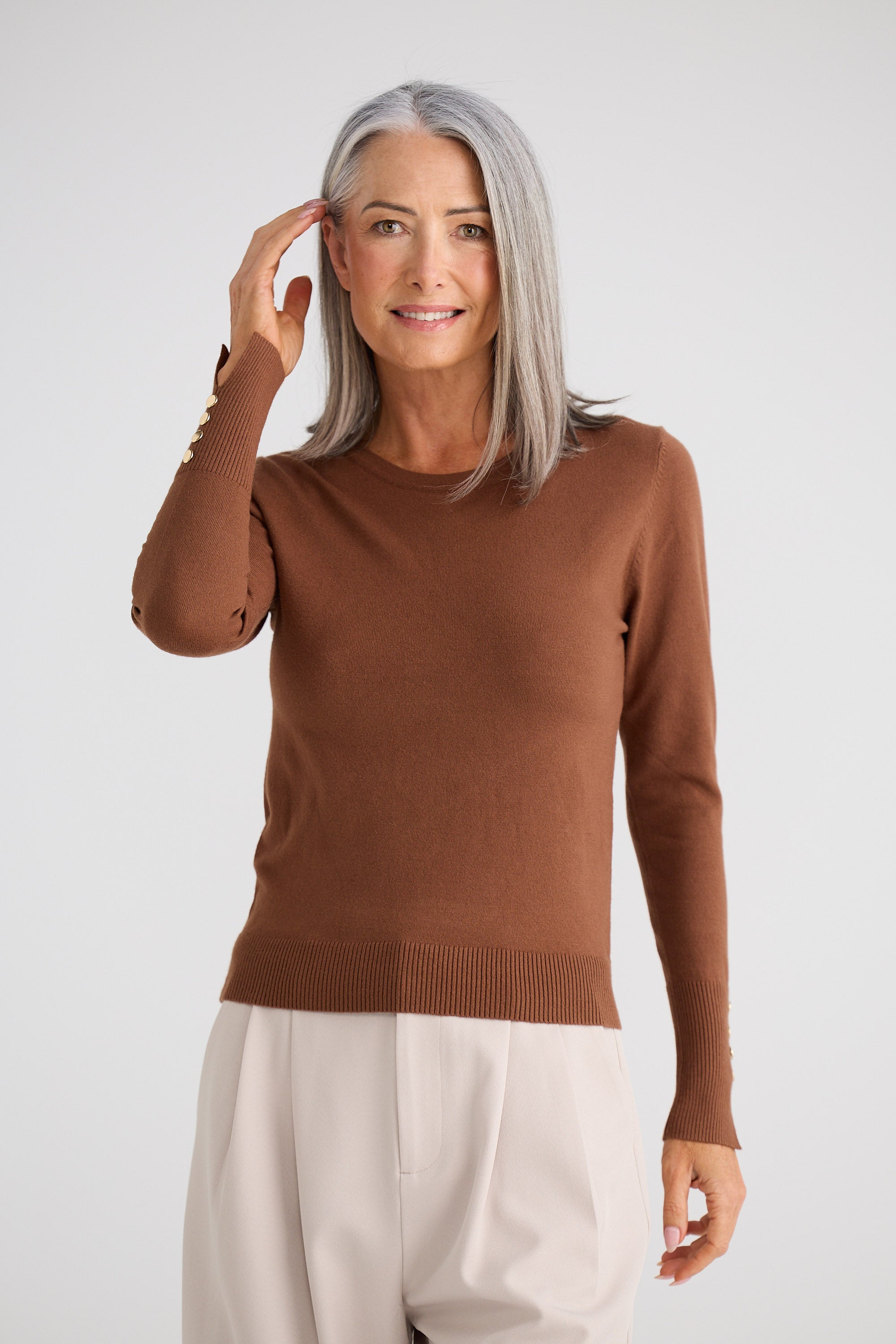 Woman wearing a brown sweater and beige pants against a white background