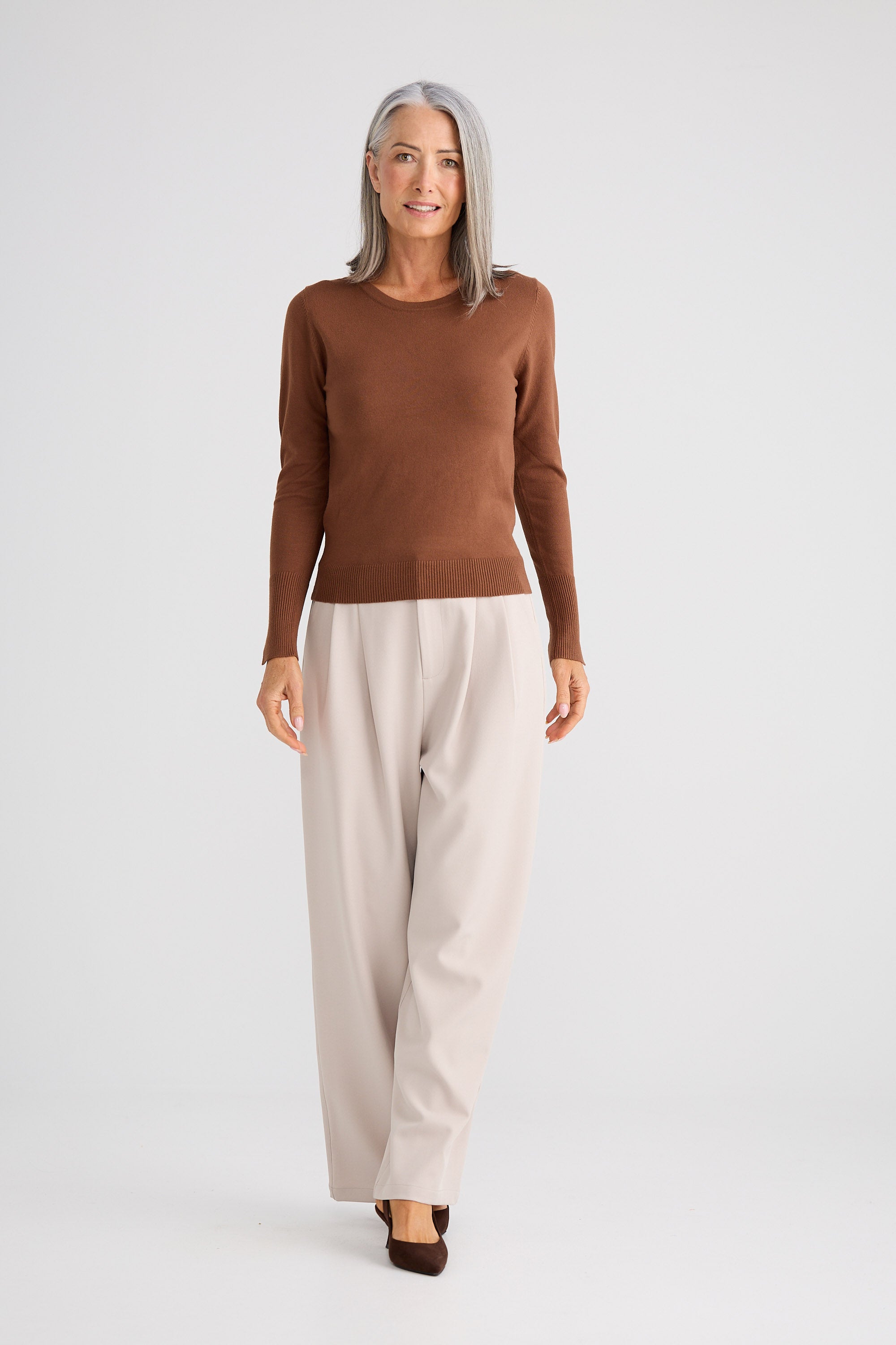 Woman wearing a brown sweater and beige pants on a white background