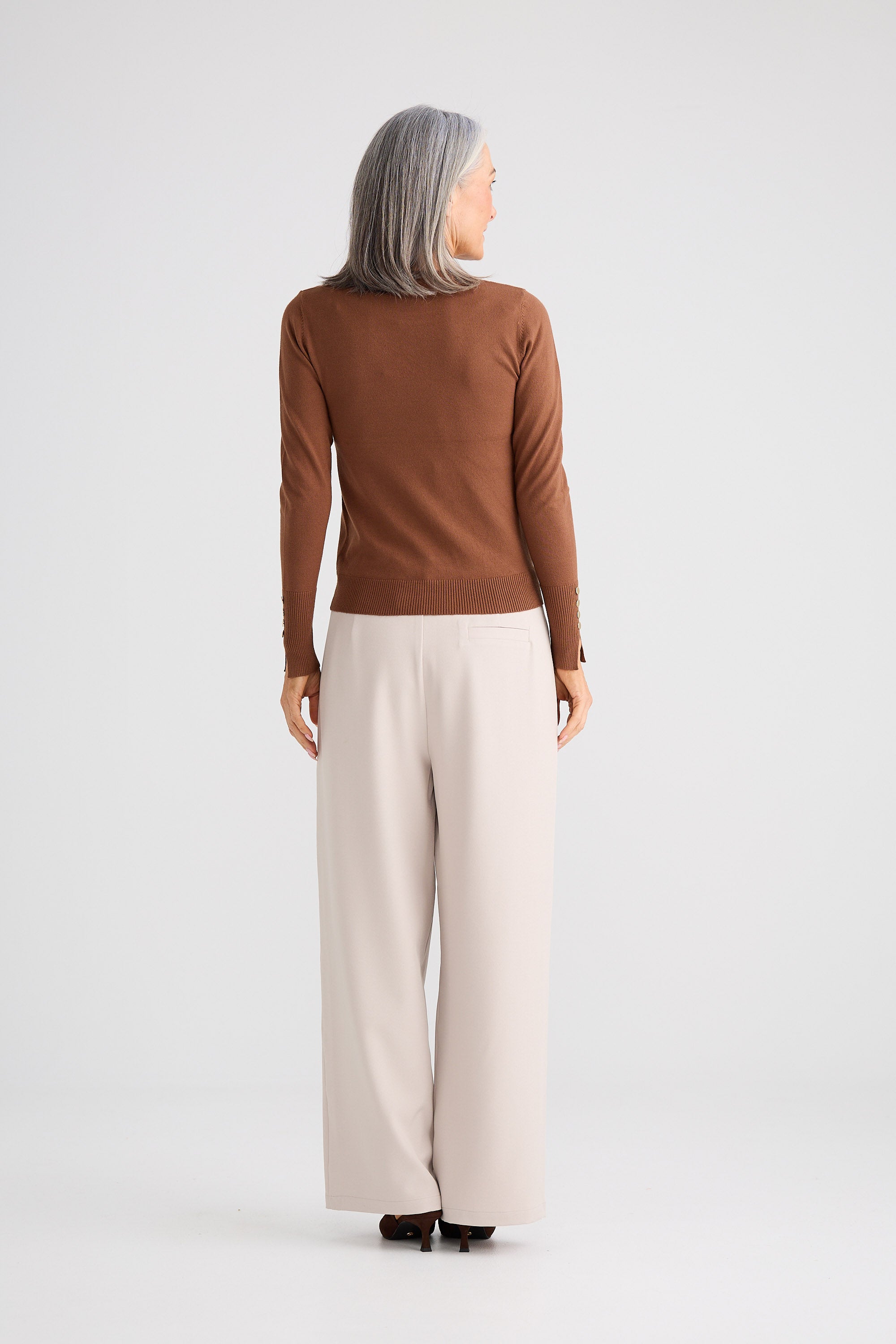 Person wearing a brown sweater and beige pants on a white background
