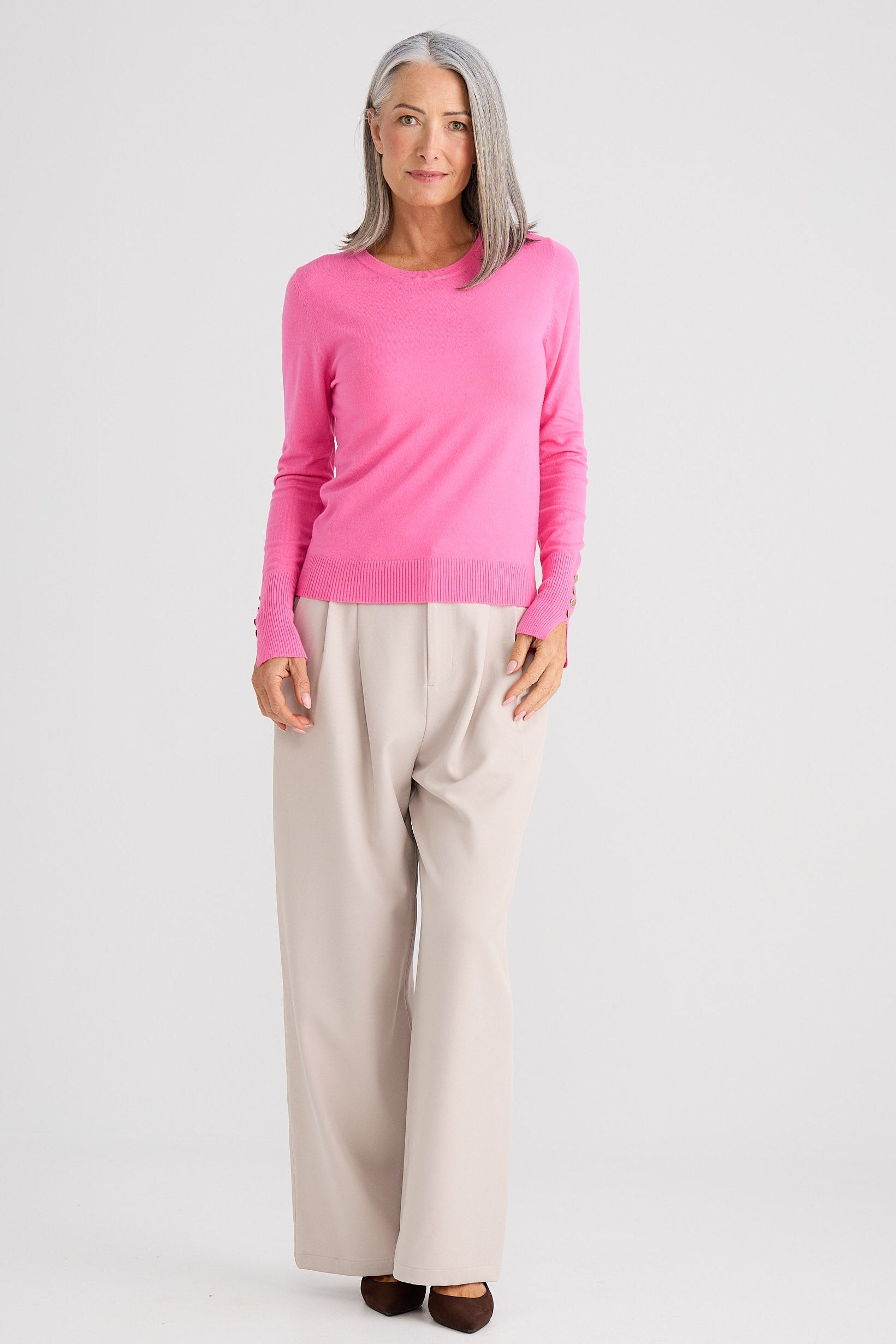 Woman wearing a pink sweater and beige pants on a white background
