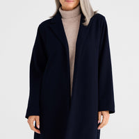 Woman wearing a navy coat over a beige sweater on a white background