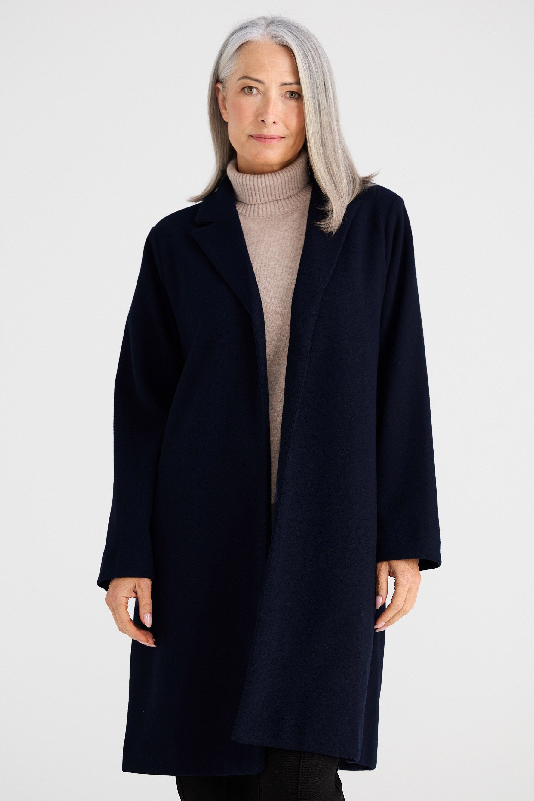 Woman wearing a navy coat over a beige sweater on a white background