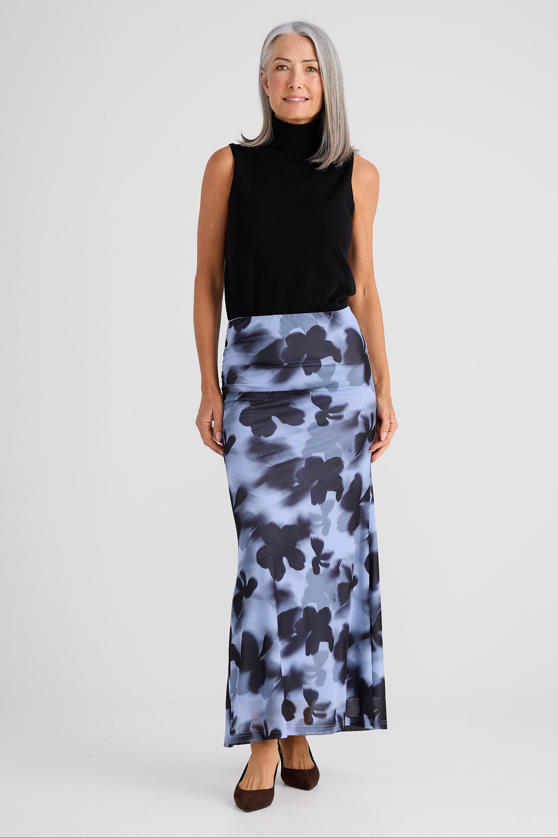 Woman wearing a black sleeveless top and a long floral skirt on a white background