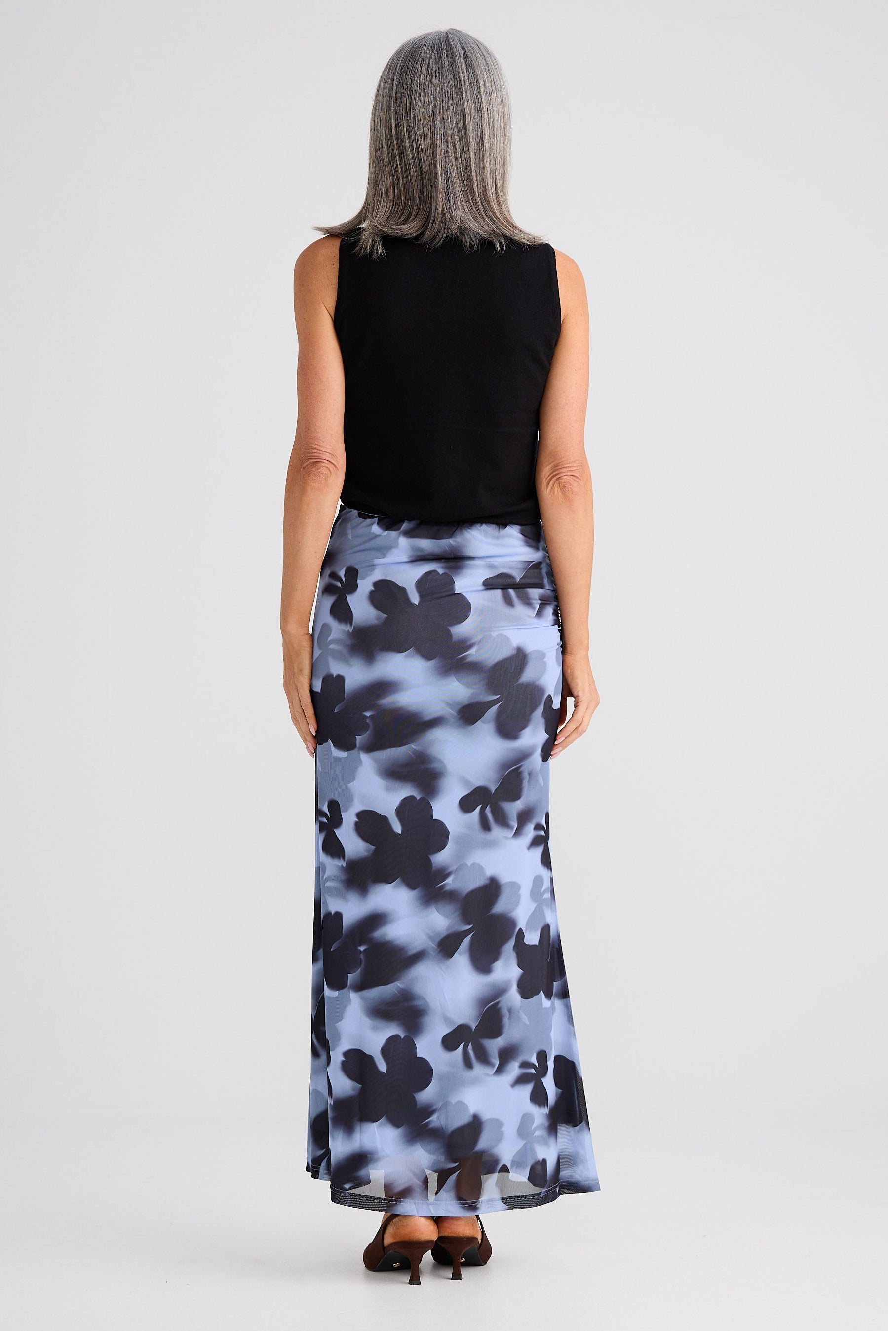 Person wearing a black sleeveless top and a long, patterned skirt on a white background