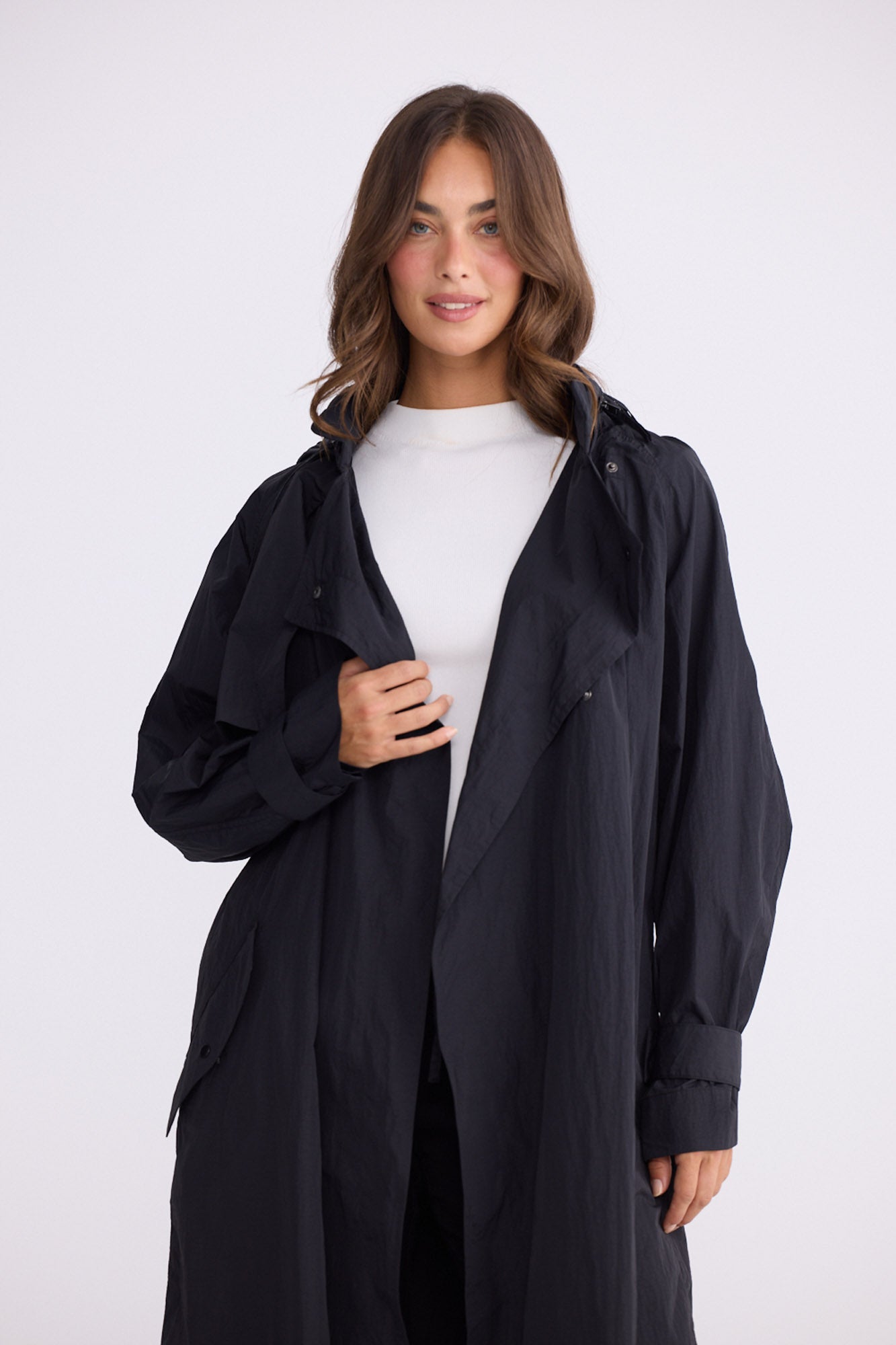 Model wearing Cressida Raincoat black coat, front pockets, alternate studio view on white background