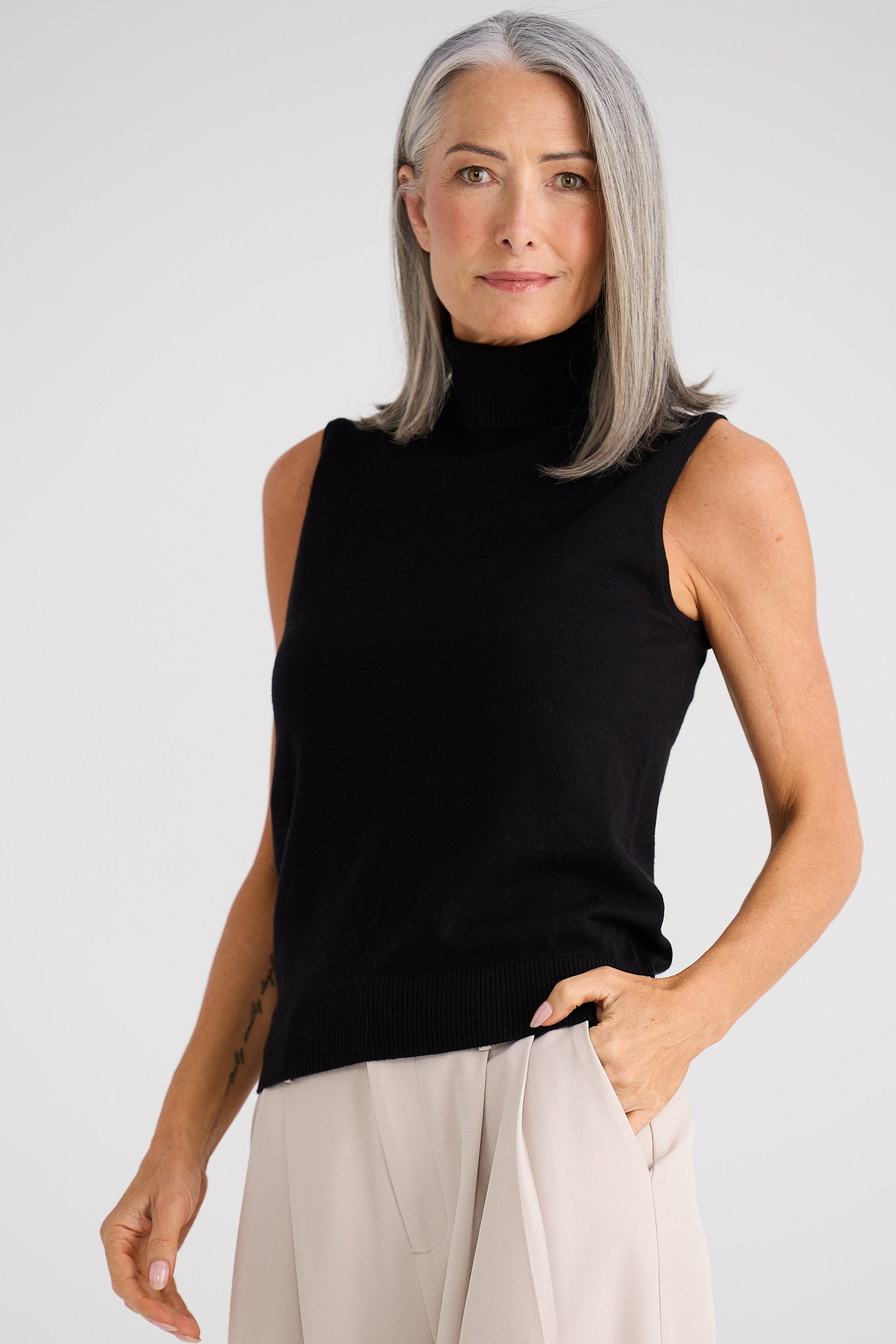 Woman wearing a black sleeveless top and beige pants against a white background