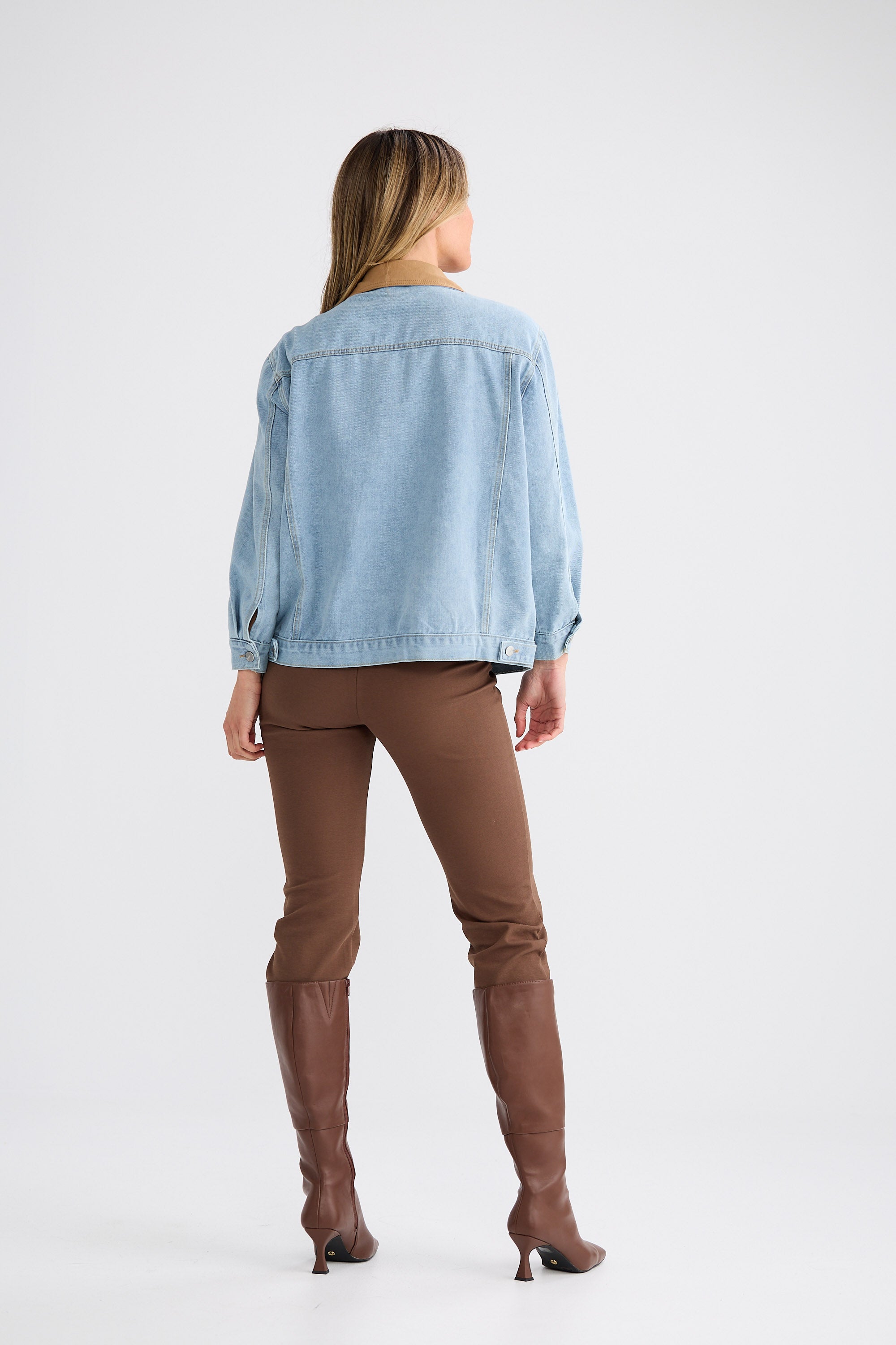Person wearing a light blue denim jacket and brown pants on a white background