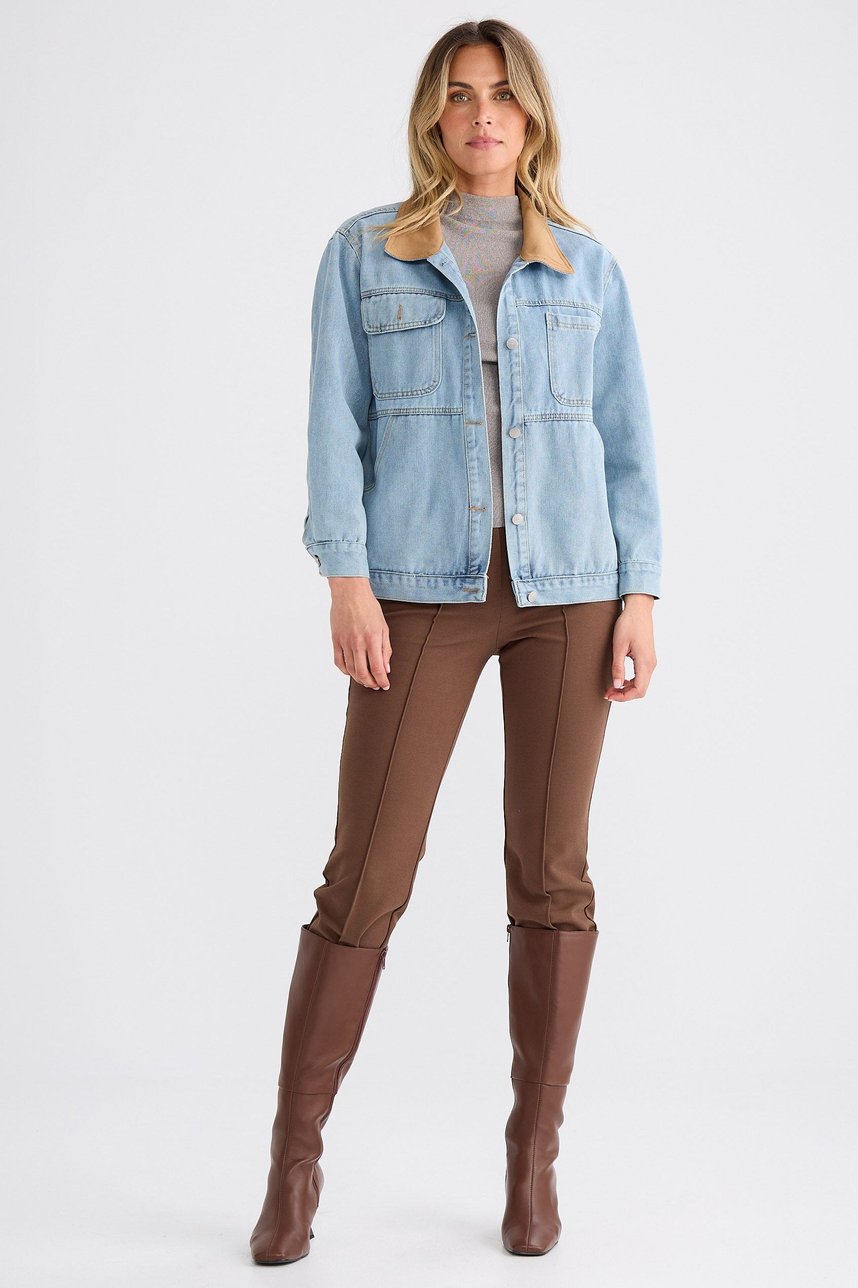 Woman wearing a light blue denim jacket, brown pants, and brown boots on a white background