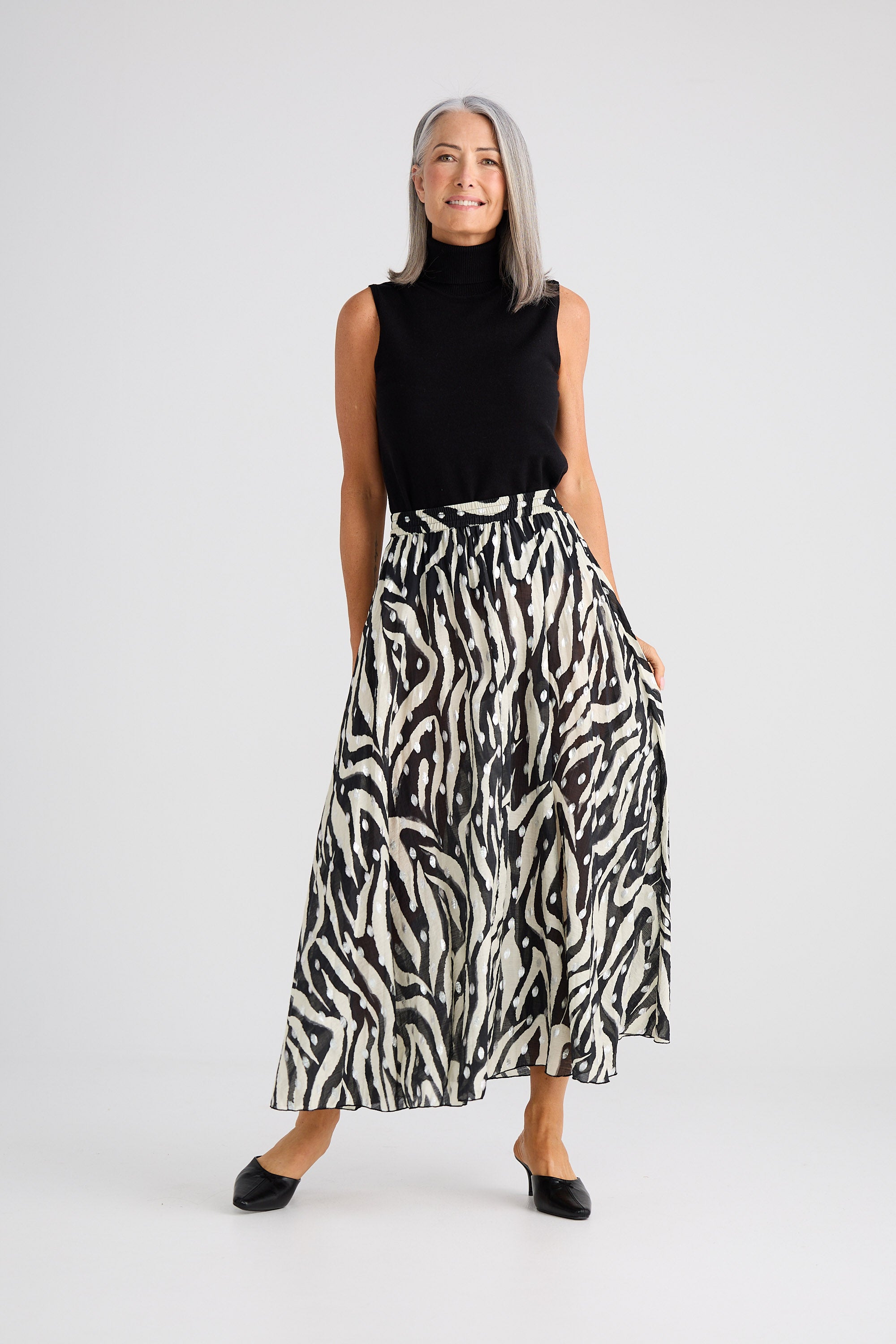 Woman wearing a black sleeveless top and zebra print skirt on a white background