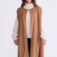 Model wearing Trini camel sleeveless cape with long fluid silhouette, alternate view on white background