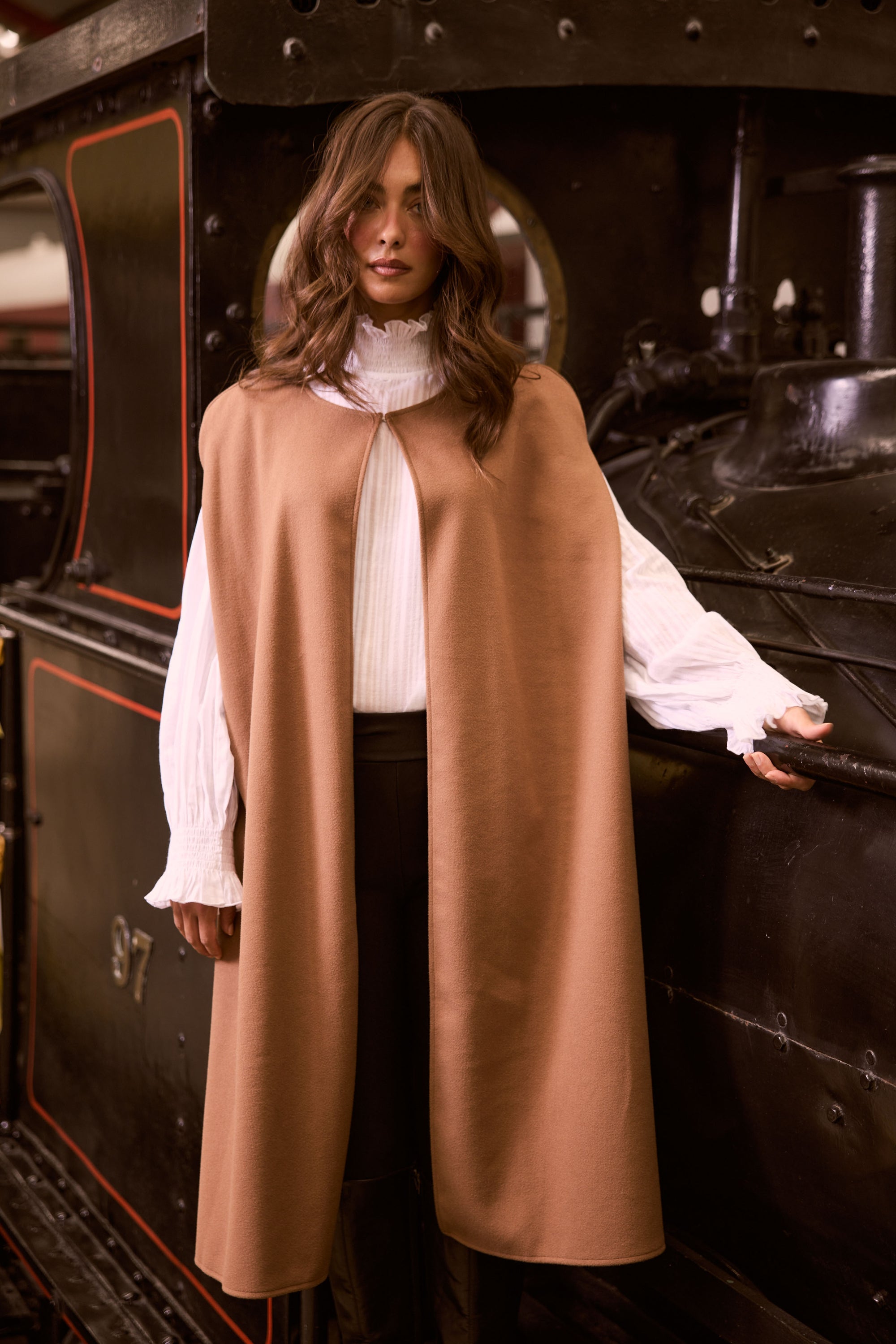Model wearing Trini camel sleeveless cape with long fluid silhouette, campaign view on white background