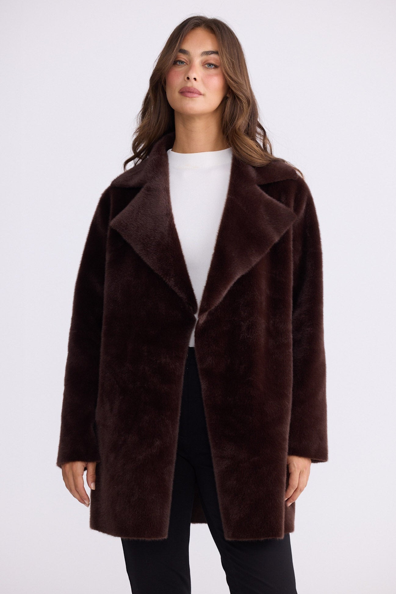 Model wearing Odette Fur Coat in brown with notched lapels and long sleeves, side view on white background