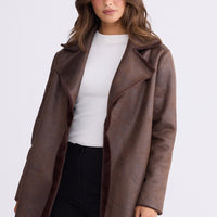 Model wearing Odette Fur Coat in brown with notched lapels and long sleeves, front view on white background