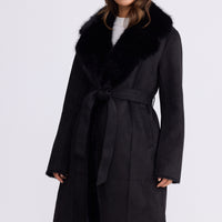 Model wearing Rosamund Fur Coat in black with notched lapels and waist tie, front view on white background