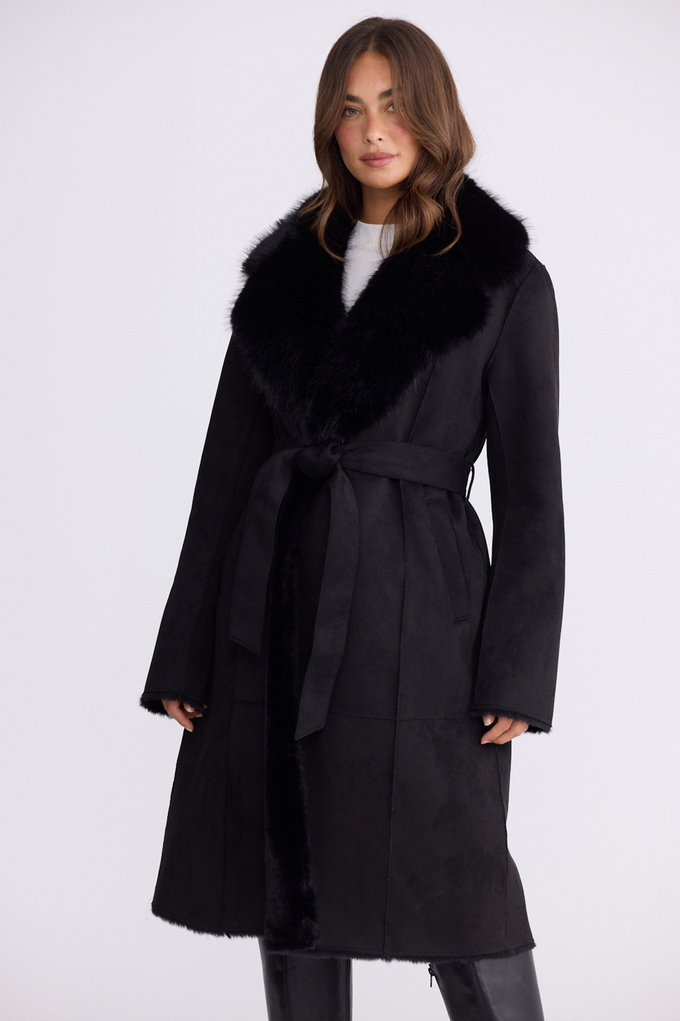 Model wearing Rosamund Fur Coat in black with notched lapels and waist tie, front view on white background