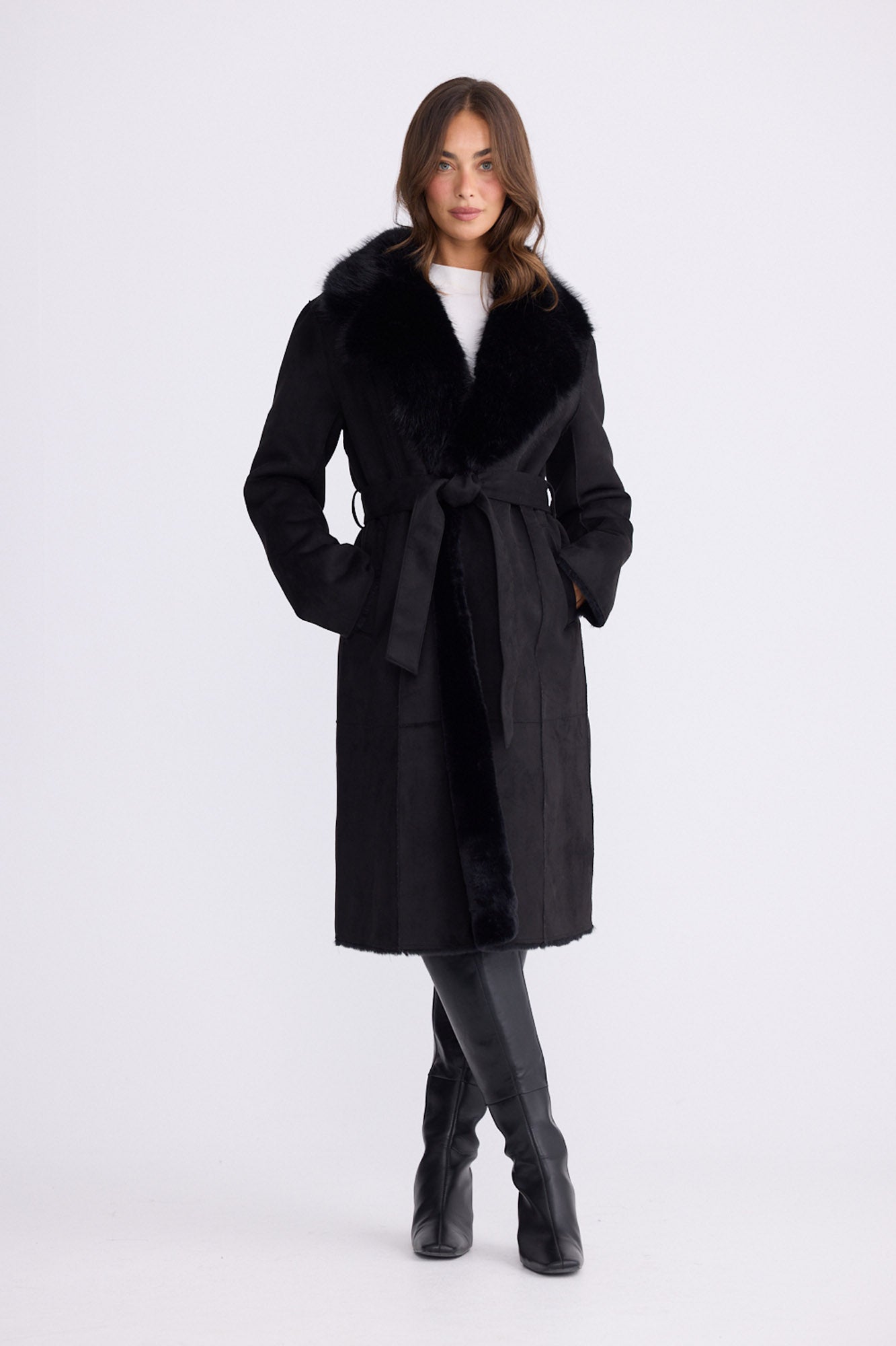 Model wearing Rosamund Fur Coat in black with notched lapels and waist tie, front view on white background