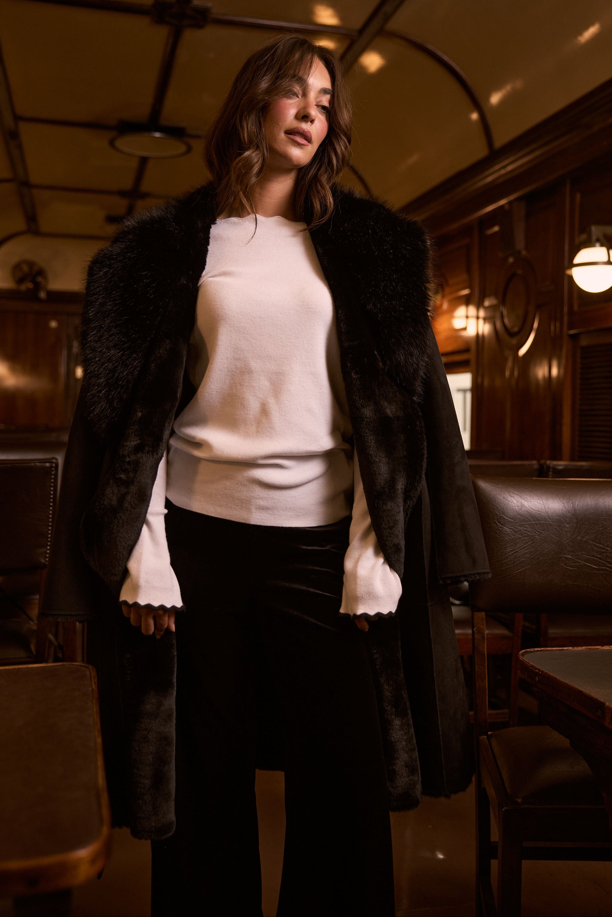 Model wearing Rosamund Fur Coat in black with notched lapels and waist tie, detail view on white background