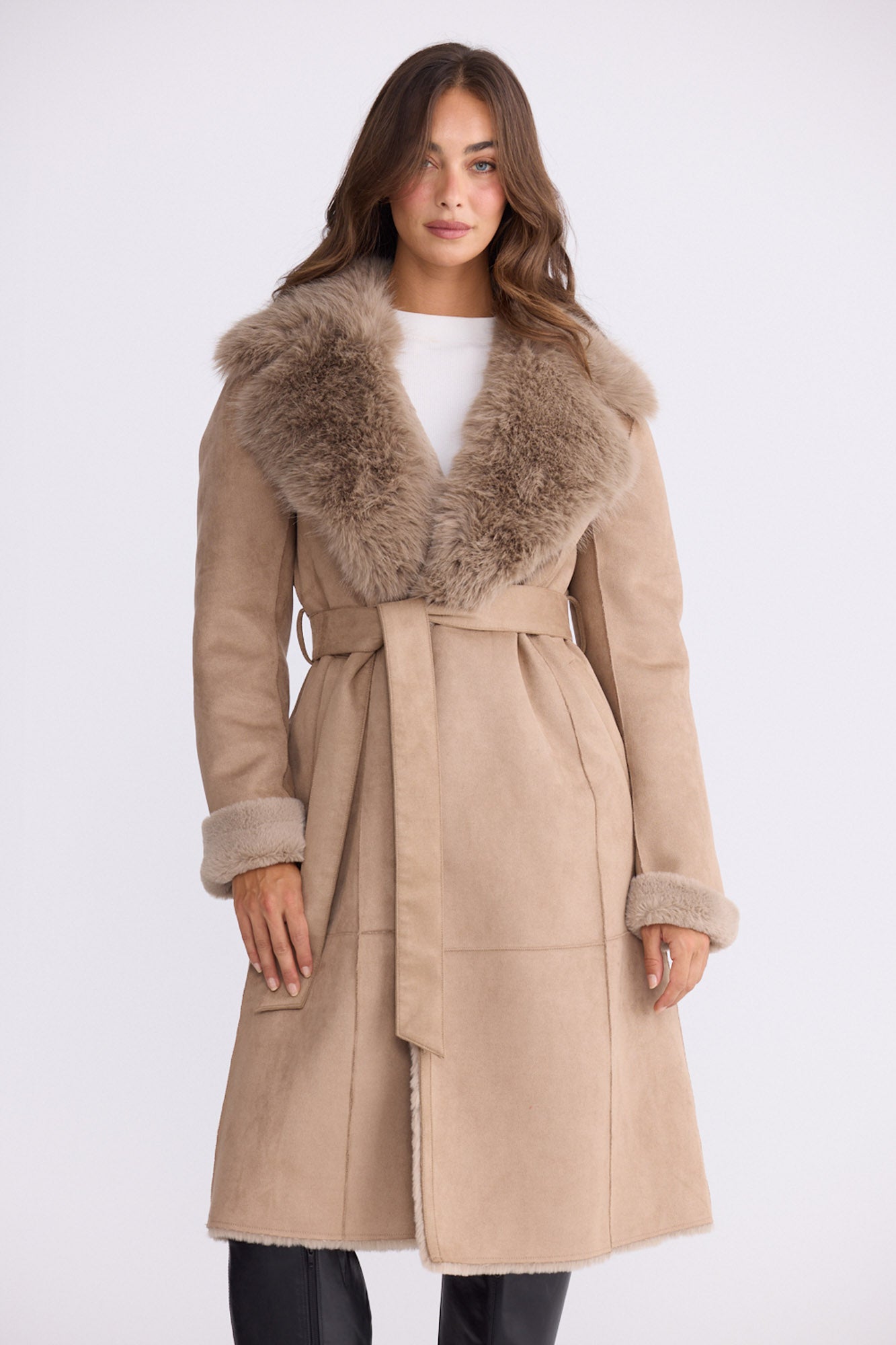 Model wearing Rosamund Fur Coat in beige with notched lapels and waist tie, side view on white background