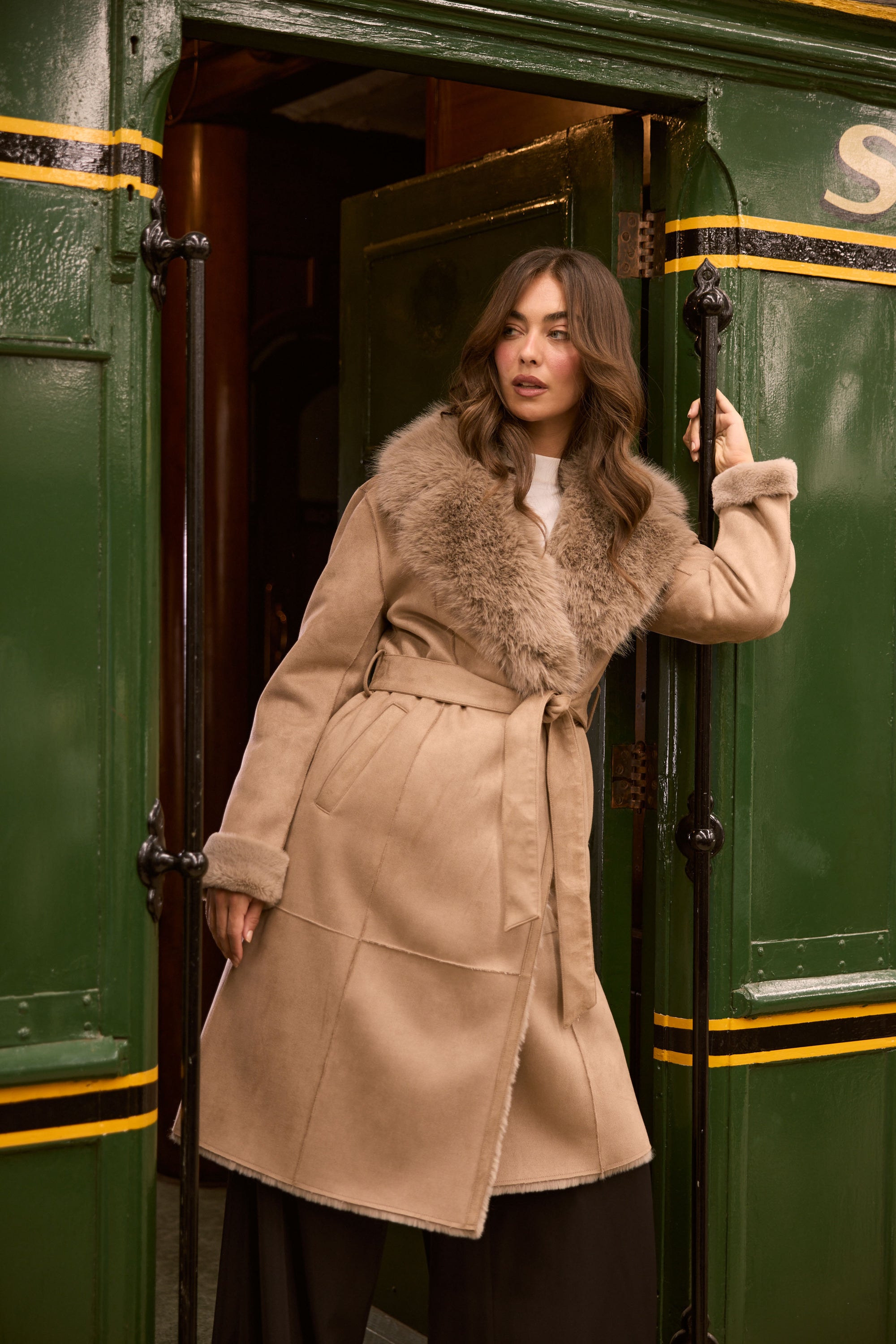 Model wearing Rosamund Fur Coat in beige with notched lapels and waist tie, detail view on white background