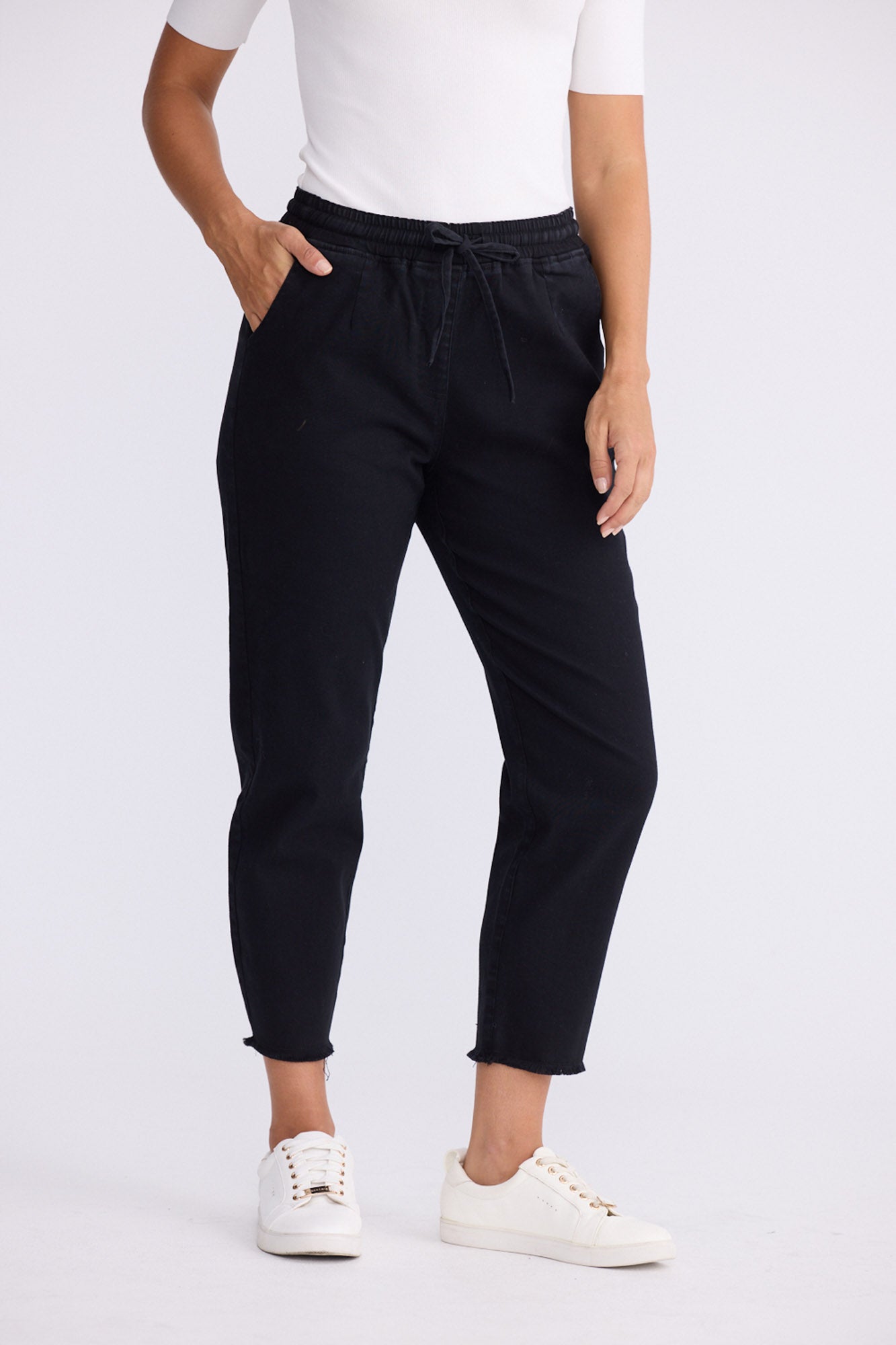 Model wearing Wayfarer black tapered pants with drawstring waist and raw hem, alternate view on white background