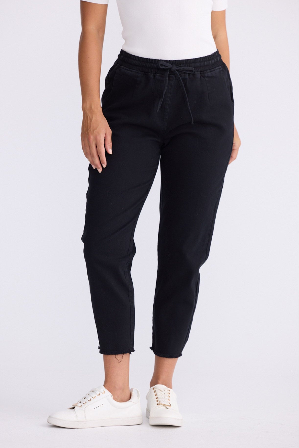 Model wearing Wayfarer black tapered pants with drawstring waist and raw hem, close-up front view on white background
