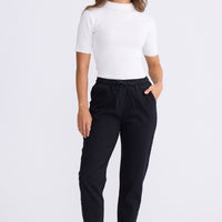 Model wearing Wayfarer black tapered pants with drawstring waist and raw hem, alternate view on white background