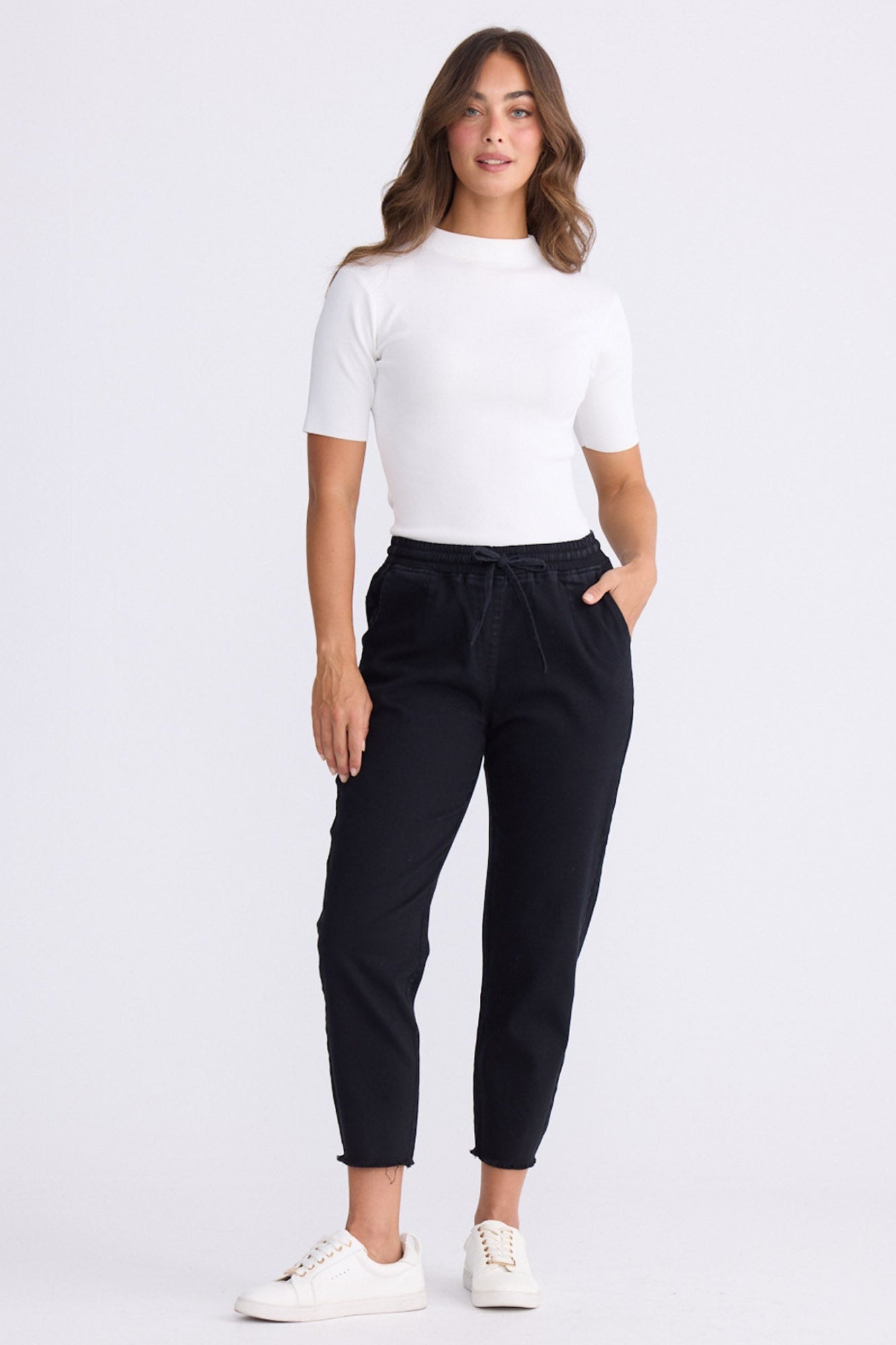 Model wearing Wayfarer black tapered pants with drawstring waist and raw hem, alternate view on white background