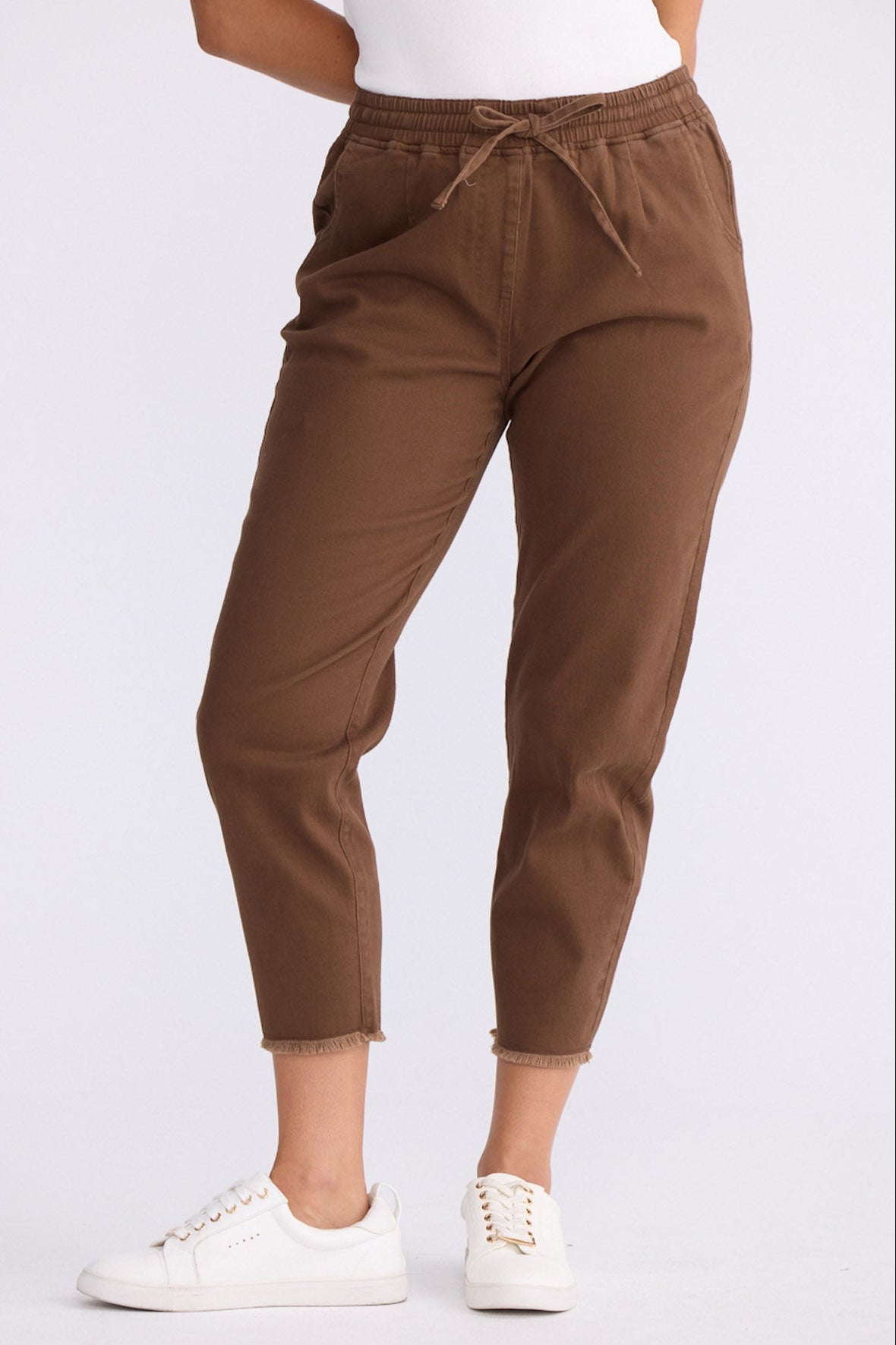 Model wearing Wayfarer chocolate tapered pants with drawstring waist and raw hem, close-up front view on white background