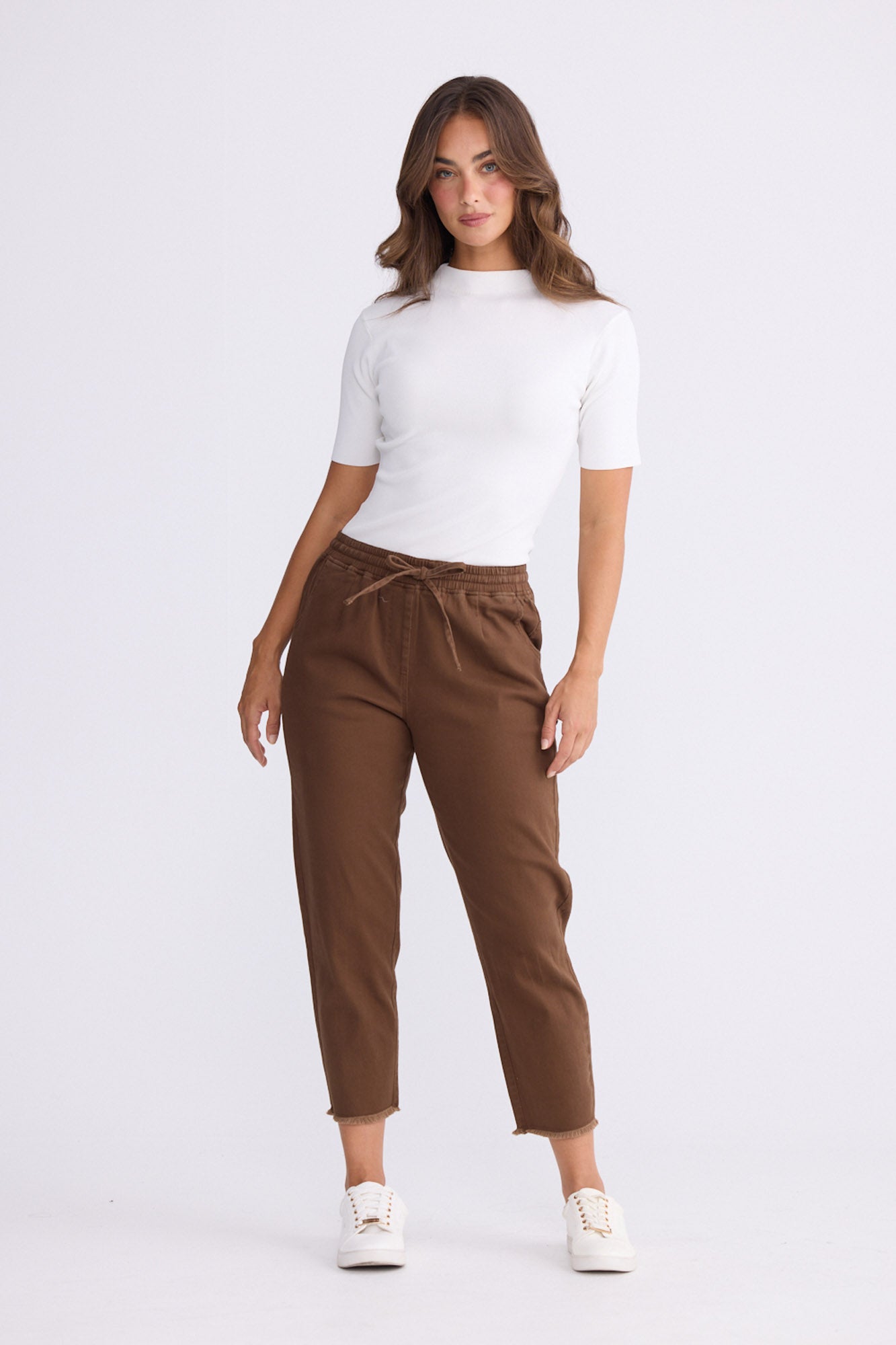 Model wearing Wayfarer chocolate tapered pants with drawstring waist and raw hem, alternate view on white background