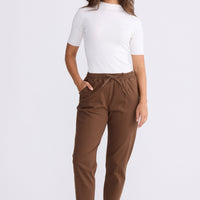 Model wearing Wayfarer chocolate tapered pants with drawstring waist and raw hem, alternate view on white background