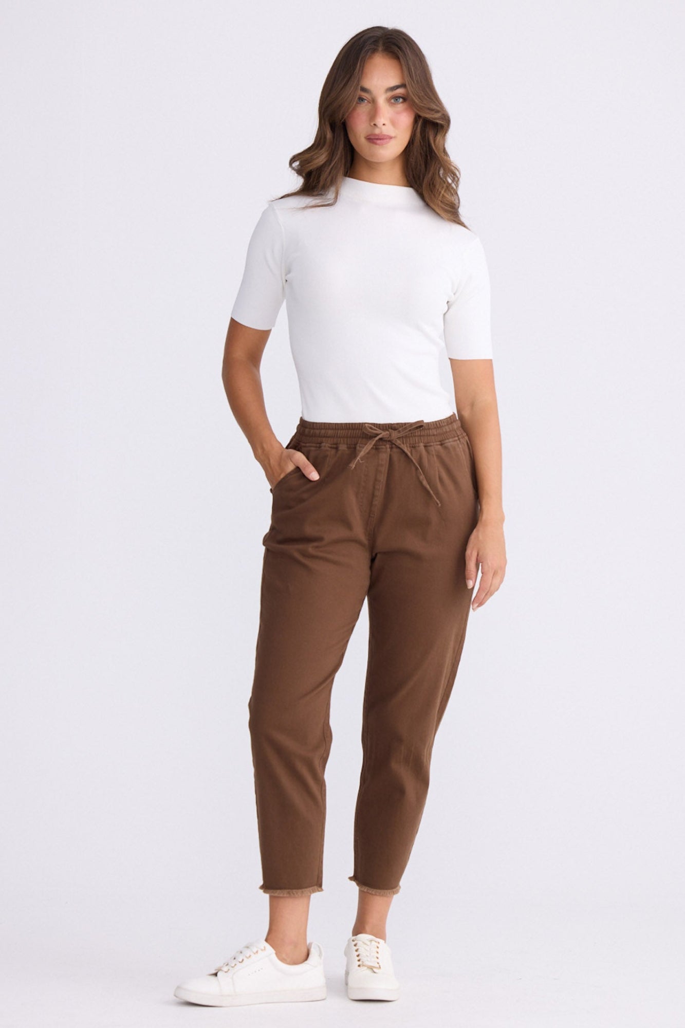 Model wearing Wayfarer chocolate tapered pants with drawstring waist and raw hem, alternate view on white background