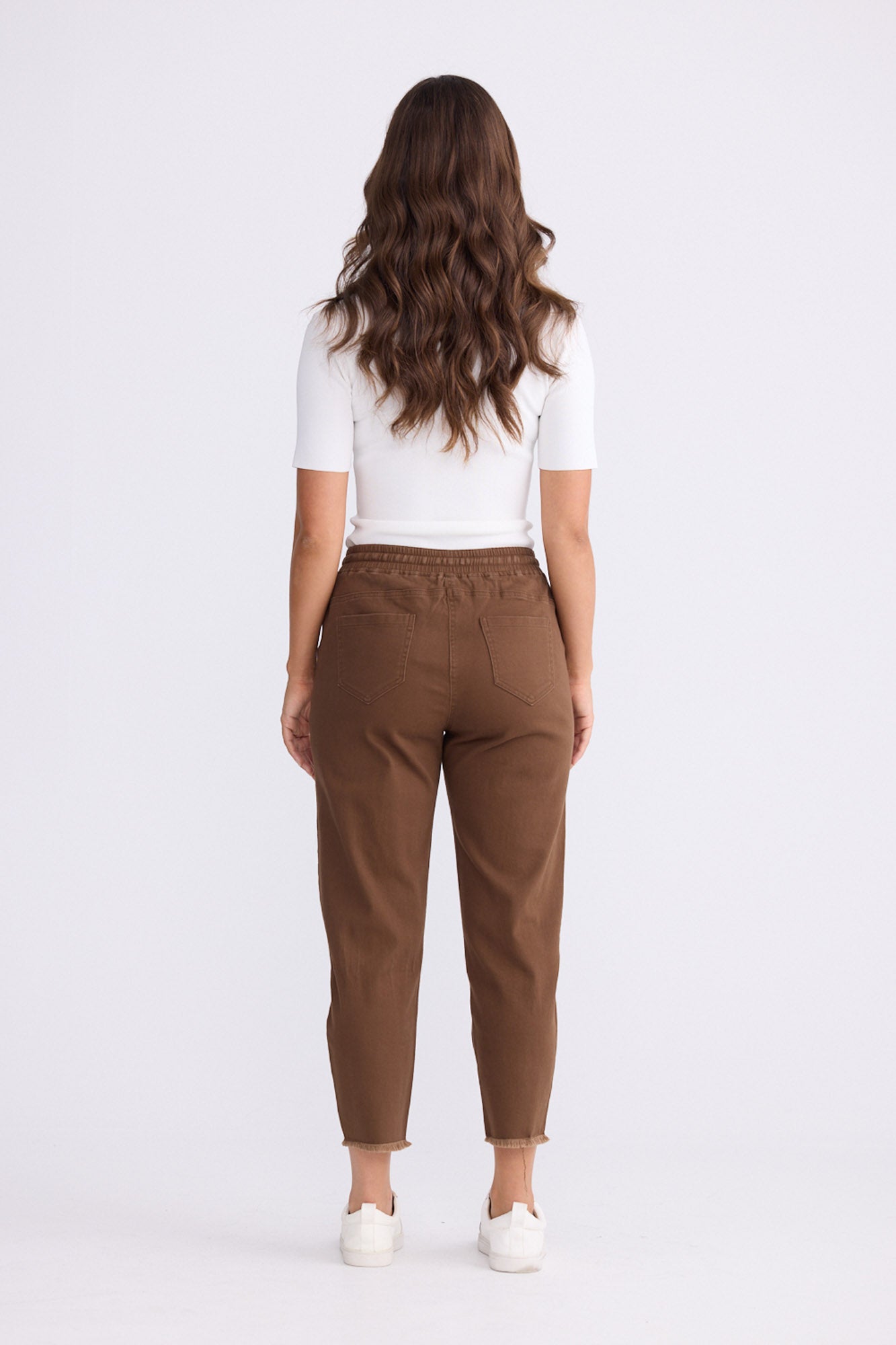 Model wearing Wayfarer chocolate tapered pants with drawstring waist and raw hem, alternate view on white background
