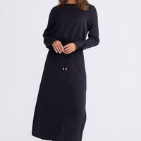 Model wearing Kensington Dress in black with boat neckline and long sleeves, back view on white background