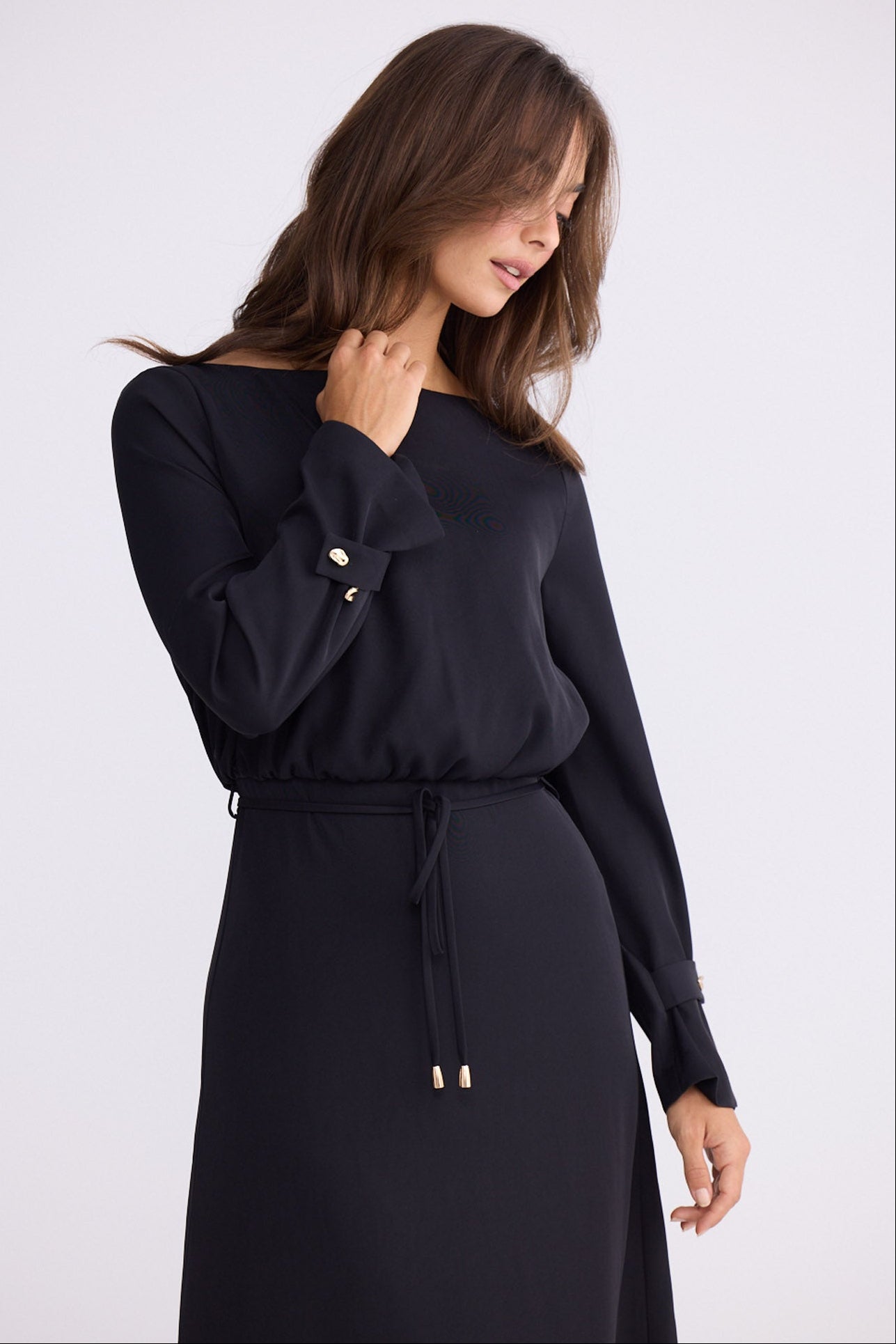 Model wearing Kensington Dress in black with boat neckline and long sleeves, front view on white background