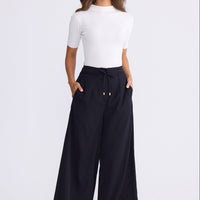 Model wearing Kensington Pant in black with waist tie and wide-leg shape, side view on white background