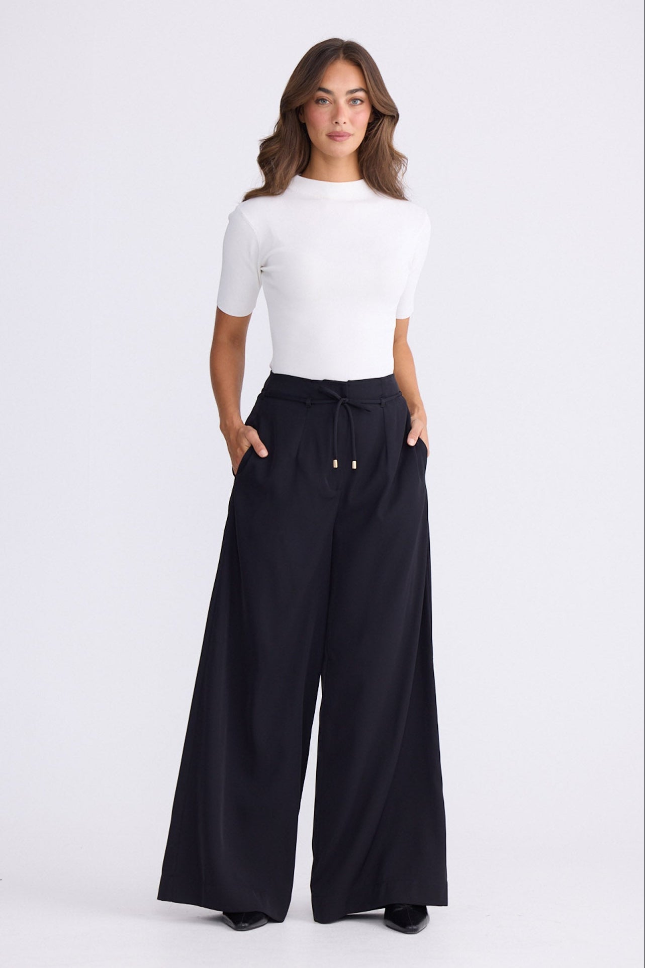 Model wearing Kensington Pant in black with waist tie and wide-leg shape, side view on white background