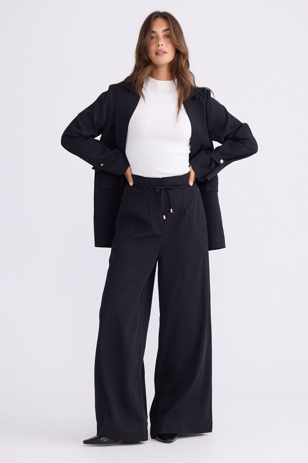 Model wearing Kensington Pant in black with waist tie and wide-leg shape, back view on white background